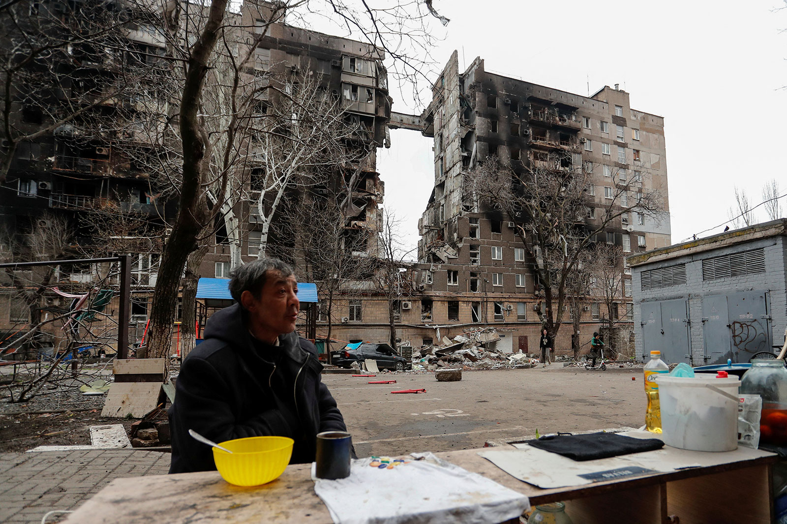 A local resident sits by a fire in the courtyard outside a damaged building in Mariupol, Ukraine, April 14.