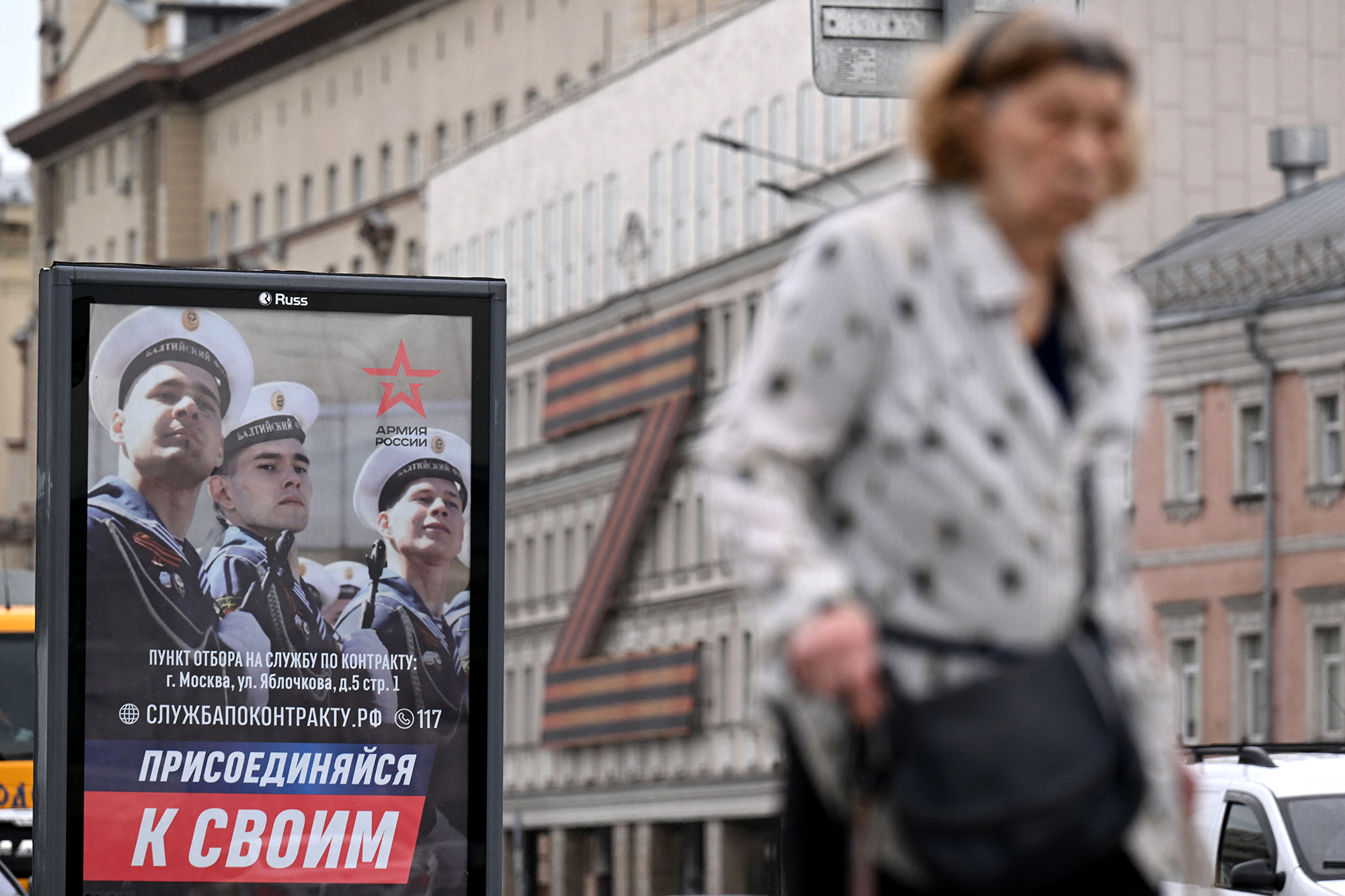 A poster promoting contract army service and reading "Join your people" with a theatre building adorned with the letter Z formed by a huge Russia's patriotic black and orange Saint George's ribbon seen in the background, in central Moscow, Russia, on July 7.