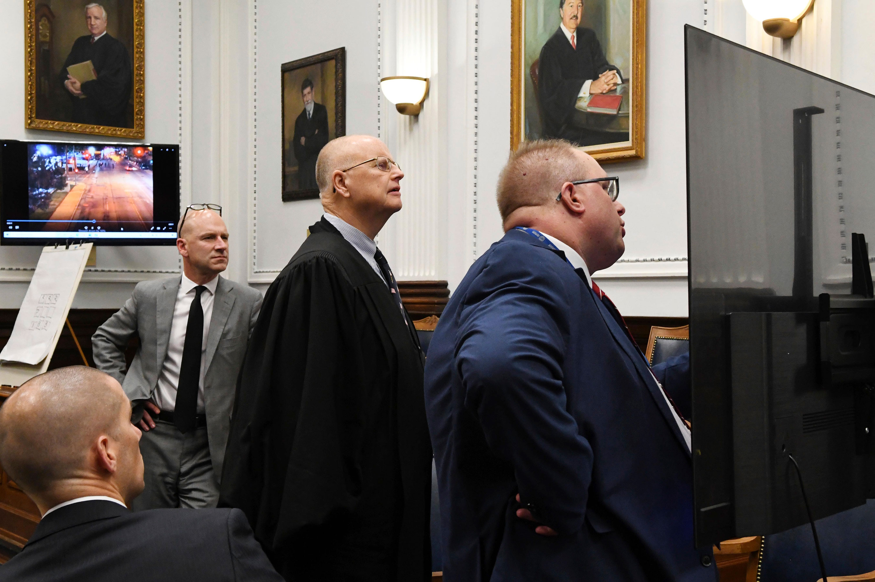 With the jury out of the room, Assistant District Attorney James Kraus, right, Judge Bruce E. Schroeder, center, and defense attorney Corey Chirafisi, rear left, look over a video monitor to examine photographic evidence during a dispute over the reliability of enlarged digital images during Kyle Rittenhouse's trial at the Kenosha County Courthouse in Kenosha, Wis., on Thursday, Nov. 11, 2021. Rittenhouse is accused of killing two people and wounding a third during a protest over police brutality in Kenosha last year.  (Mark Hertzberg/Pool Photo via AP)