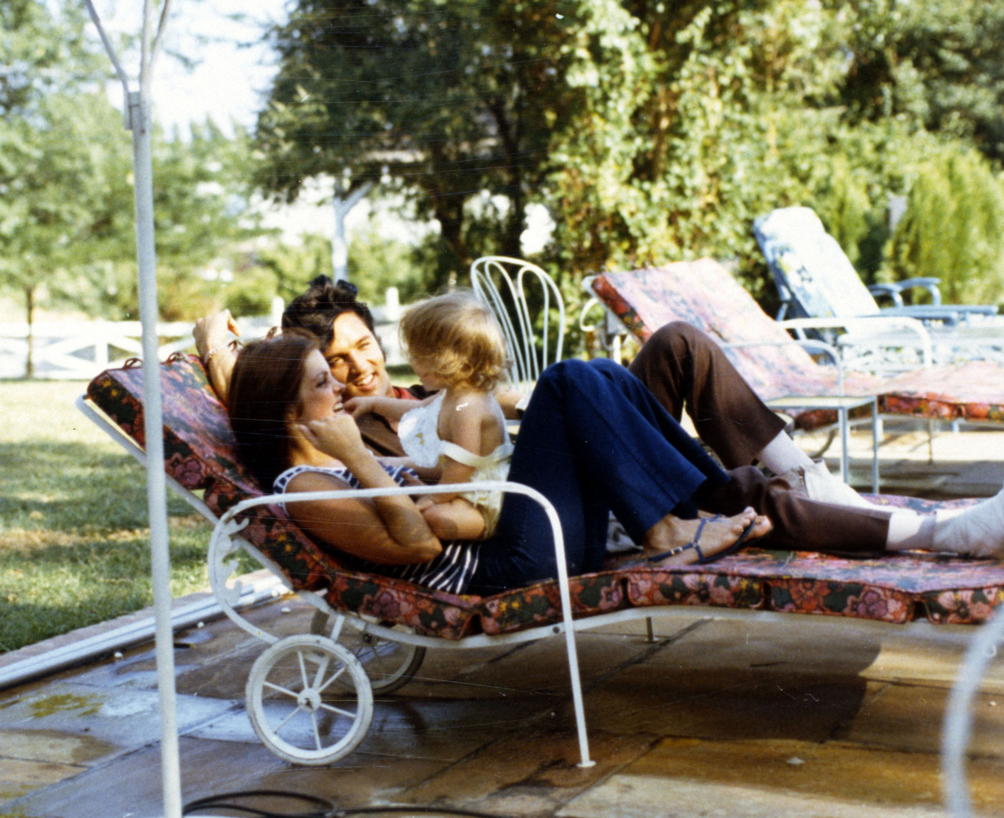 Lisa Marie Presley sits on her mother's lap while enjoying a day with her parents. 
