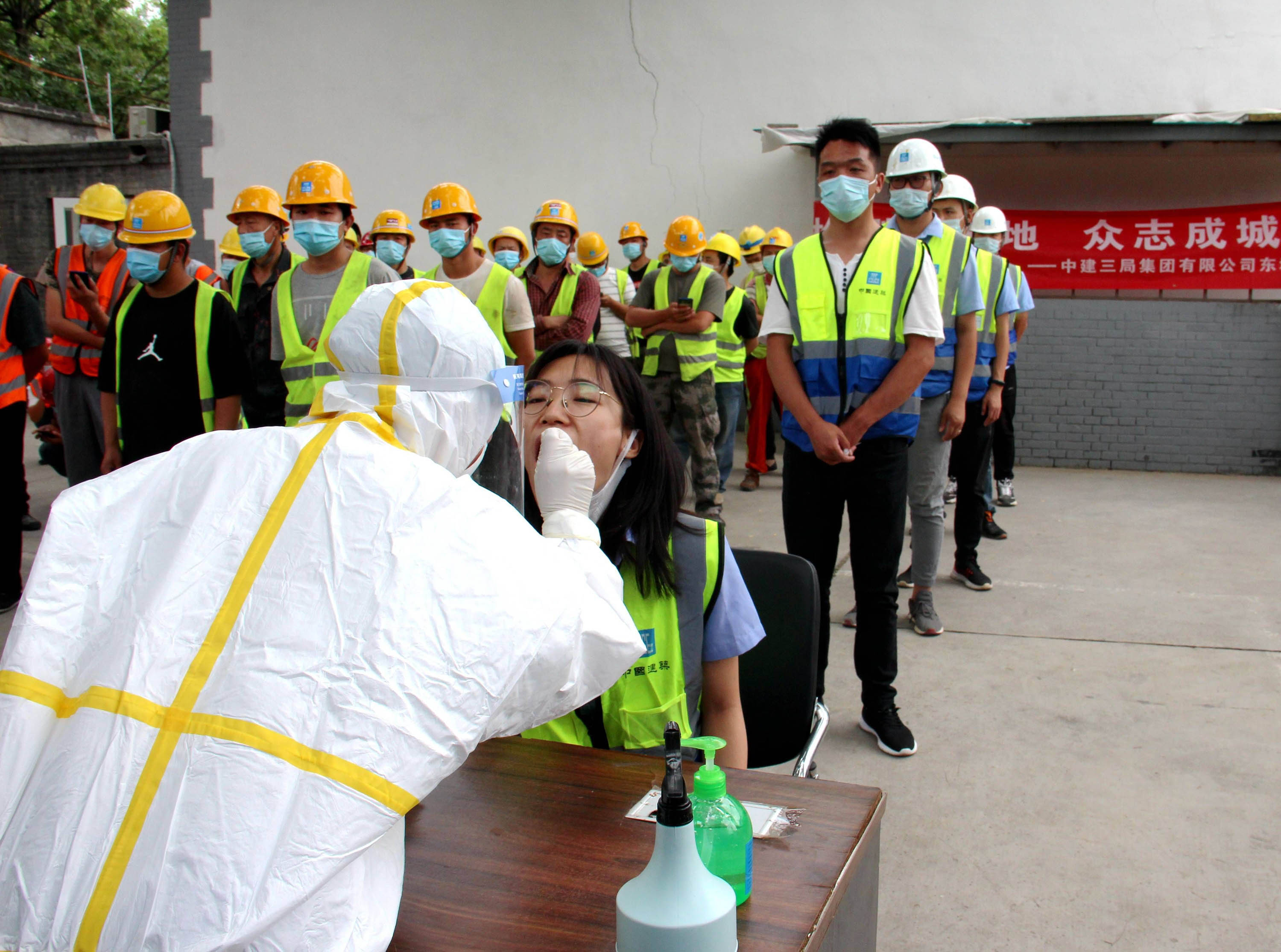 A medical worker collects throat swabs from construction workers at a construction site in Beijing on June 17.