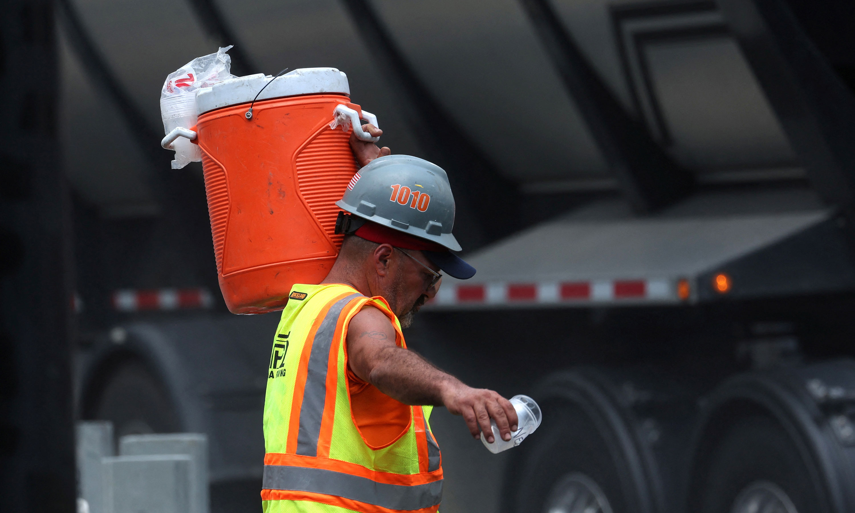 A worker carries a cooler of ice water to a road paving crew in New York on July 27. 