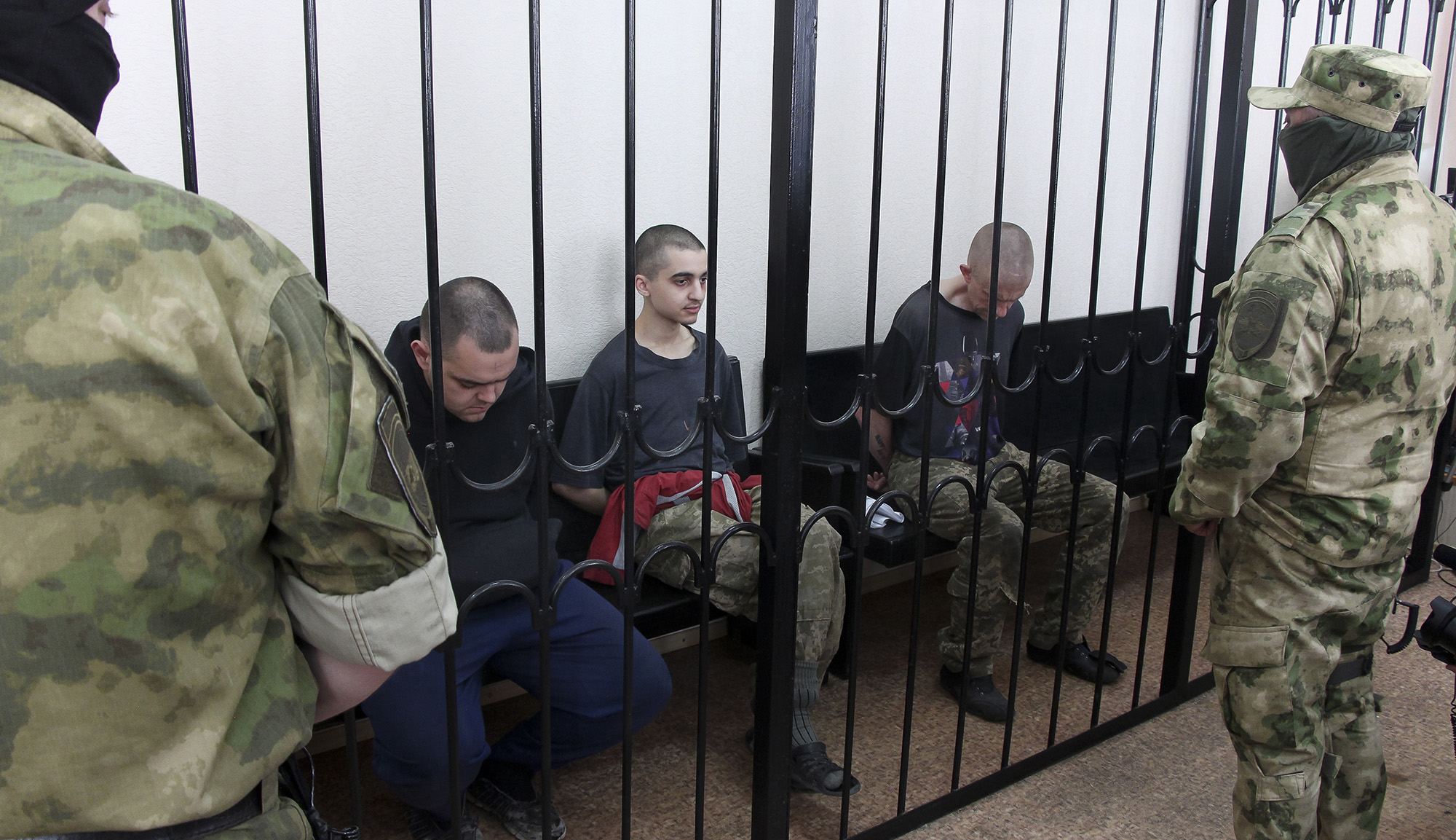 Two British citizens Aiden Aslin, left, and Shaun Pinner, right, and Moroccan Saaudun Brahim, center, sit behind bars in a courtroom in Donetsk, in the territory which is under the Government of the Donetsk People's Republic control, eastern Ukraine, on June 9.