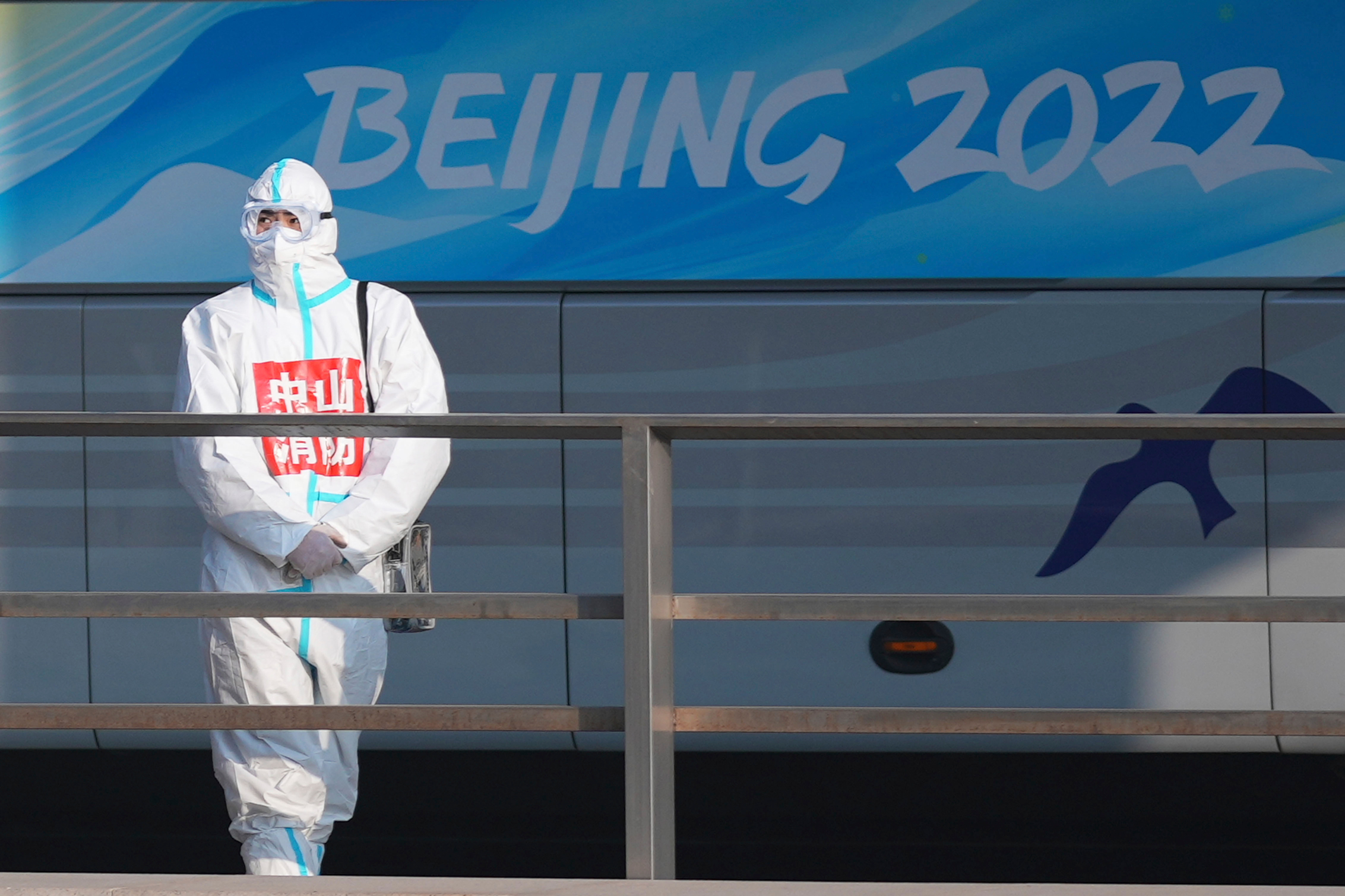 Authority personnel wearing a protective suit watches as a media bus stands by for people arriving at the Beijing Capital International Airport on Wednesday, January 5.