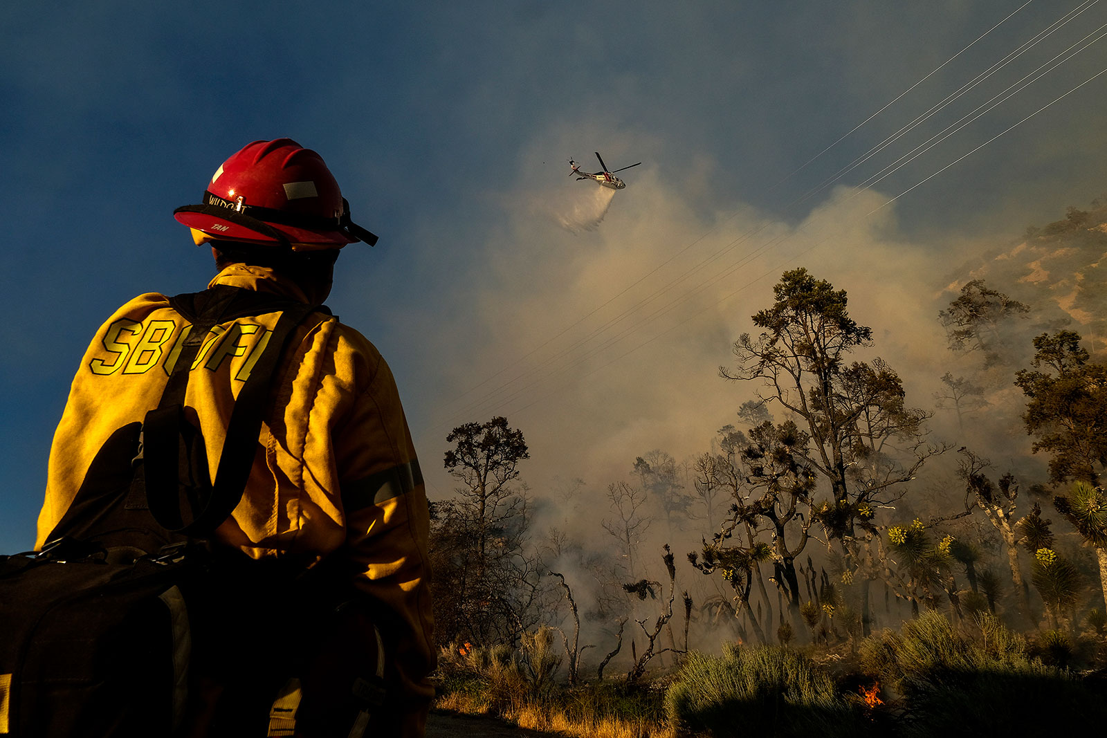 A firefighter watches a helicopter drop water on the Sheep Fire in Wrightwood, California, on Sunday, June 12.