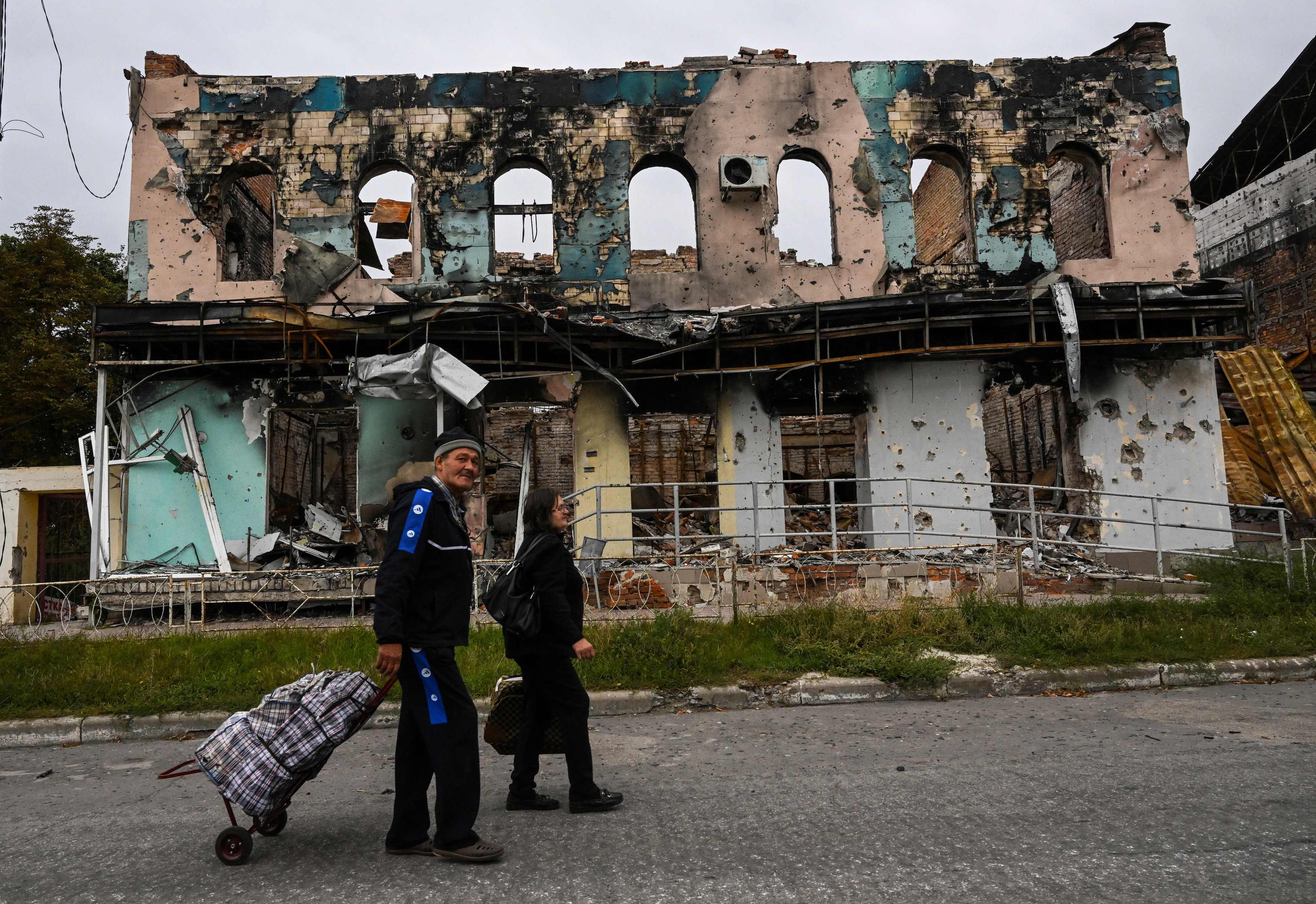 A couple wheels suitcases as they walk in front of a destroyed building in Izyum, Kharkiv Oblast on September 11.