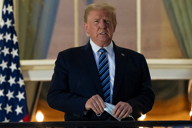 President Donald Trump holds his mask after removing it from his face as he stands on the Blue Room Balcony upon returning to the White House in Washington from the Walter Reed National Military Medical Center in Bethesda, Md. on Monday, Oct. 5, 2020.