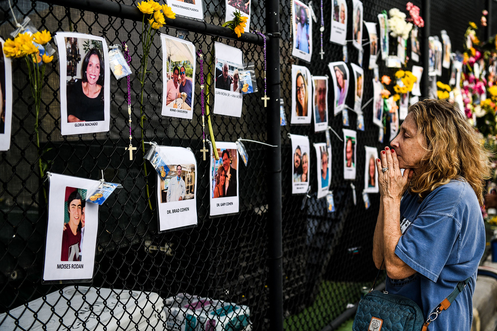 A woman prays in front of photos at the makeshift memorial for the victims of the building collapse, near the site of the accident in Surfside, Florida, north of Miami Beach on June 27.