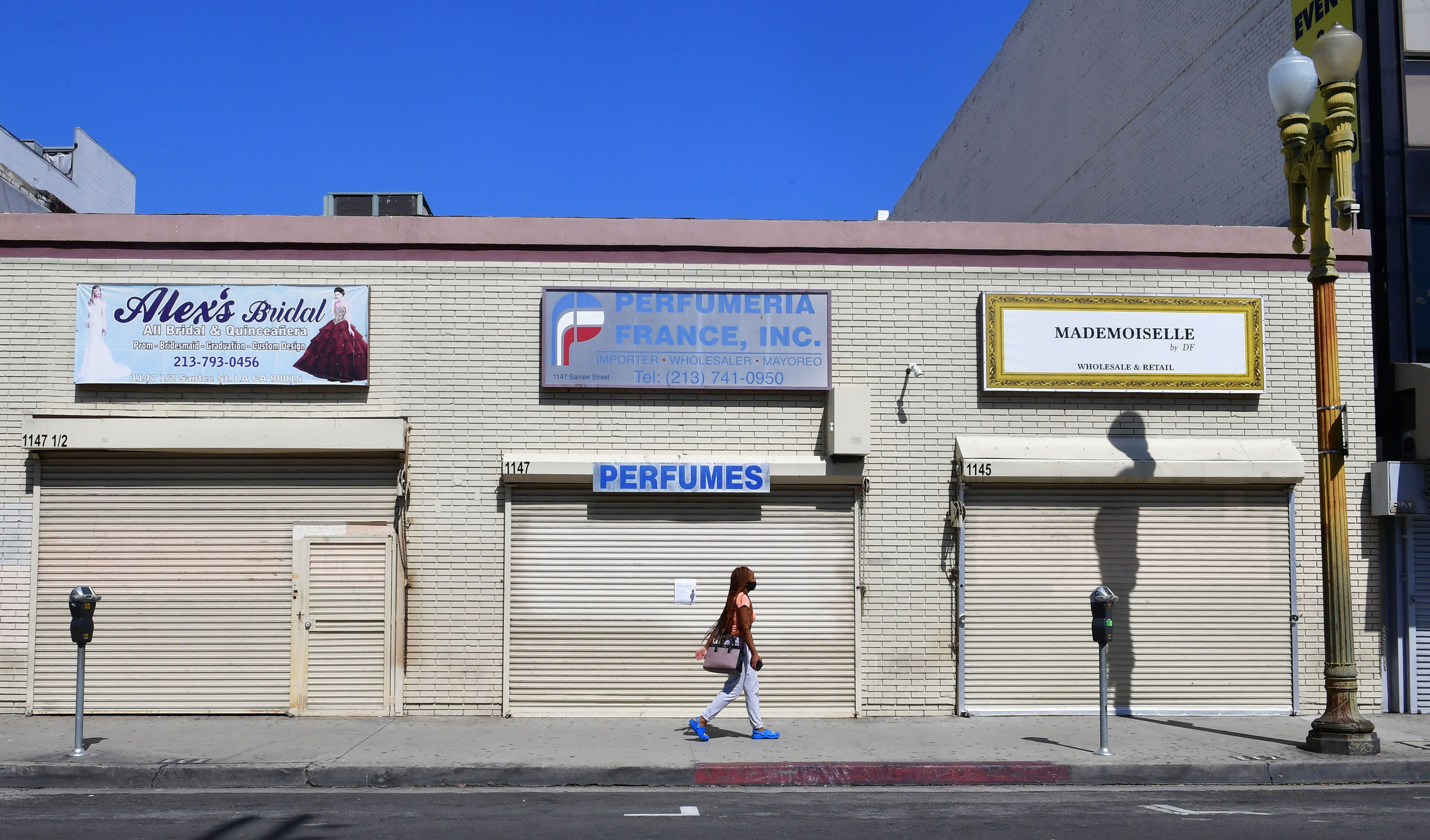 A woman walks past closed shopfronts in what would be a normally busy fashion district in Los Angeles on May 4.
