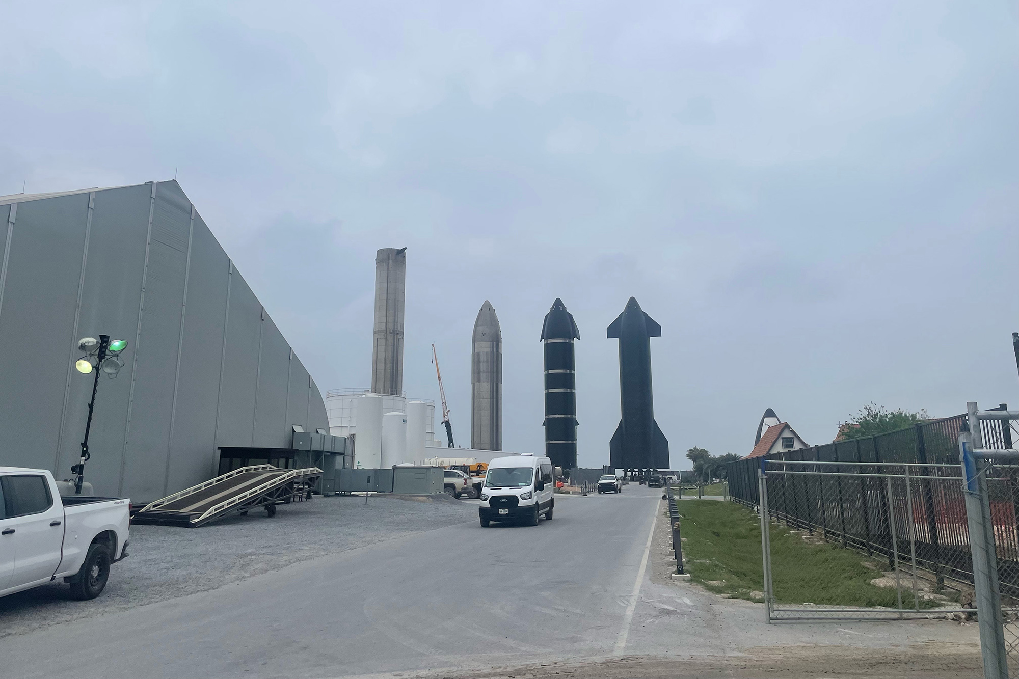 A rocket booster and three Starship spacecraft are lined up near massive assembly buildings at SpaceX's Starbase fascilities in South Texas.