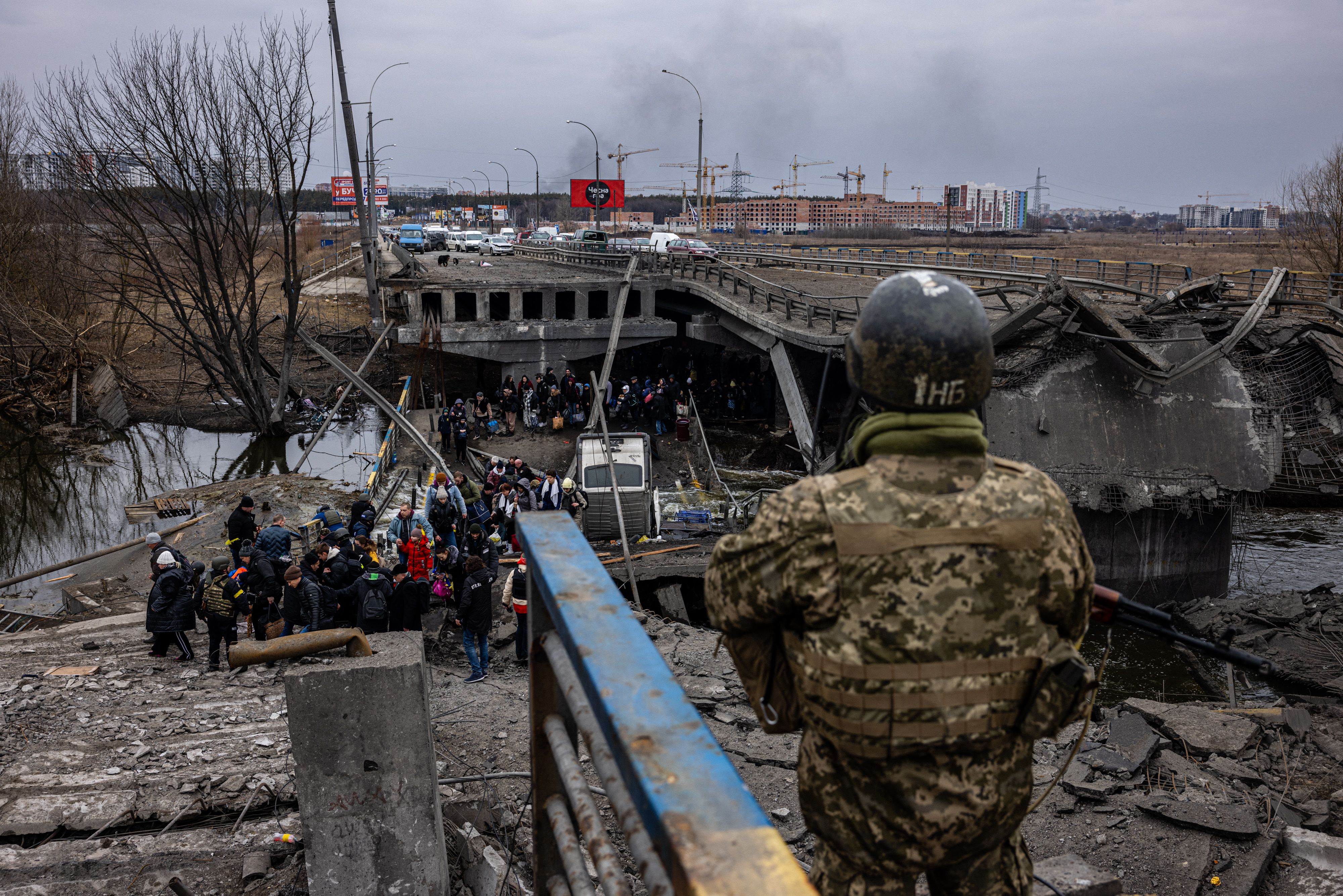 A Ukrainian serviceman looks on as evacuees cross a destroyed bridge as they flee the city of Irpin, Ukraine, on March 7.