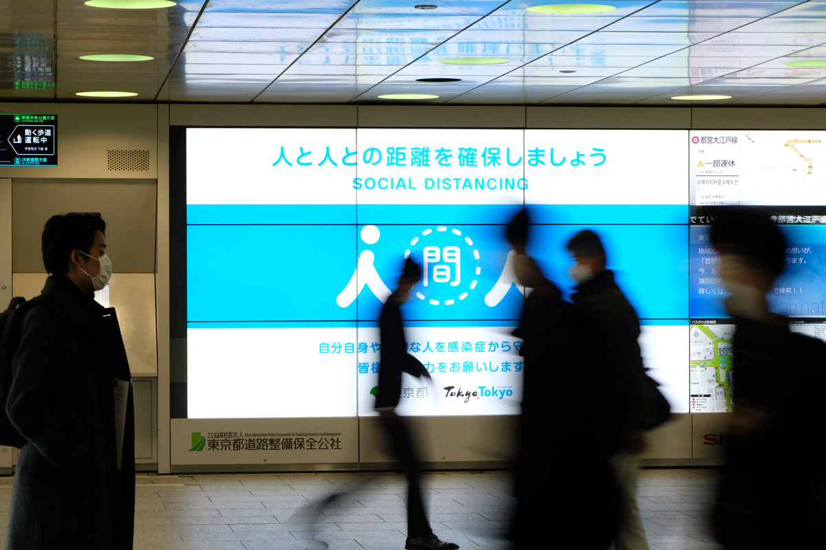People walk past a public service display promoting social distancing at a concourse leading to the terminal station in Tokyo's Shinjuku district on January 6.