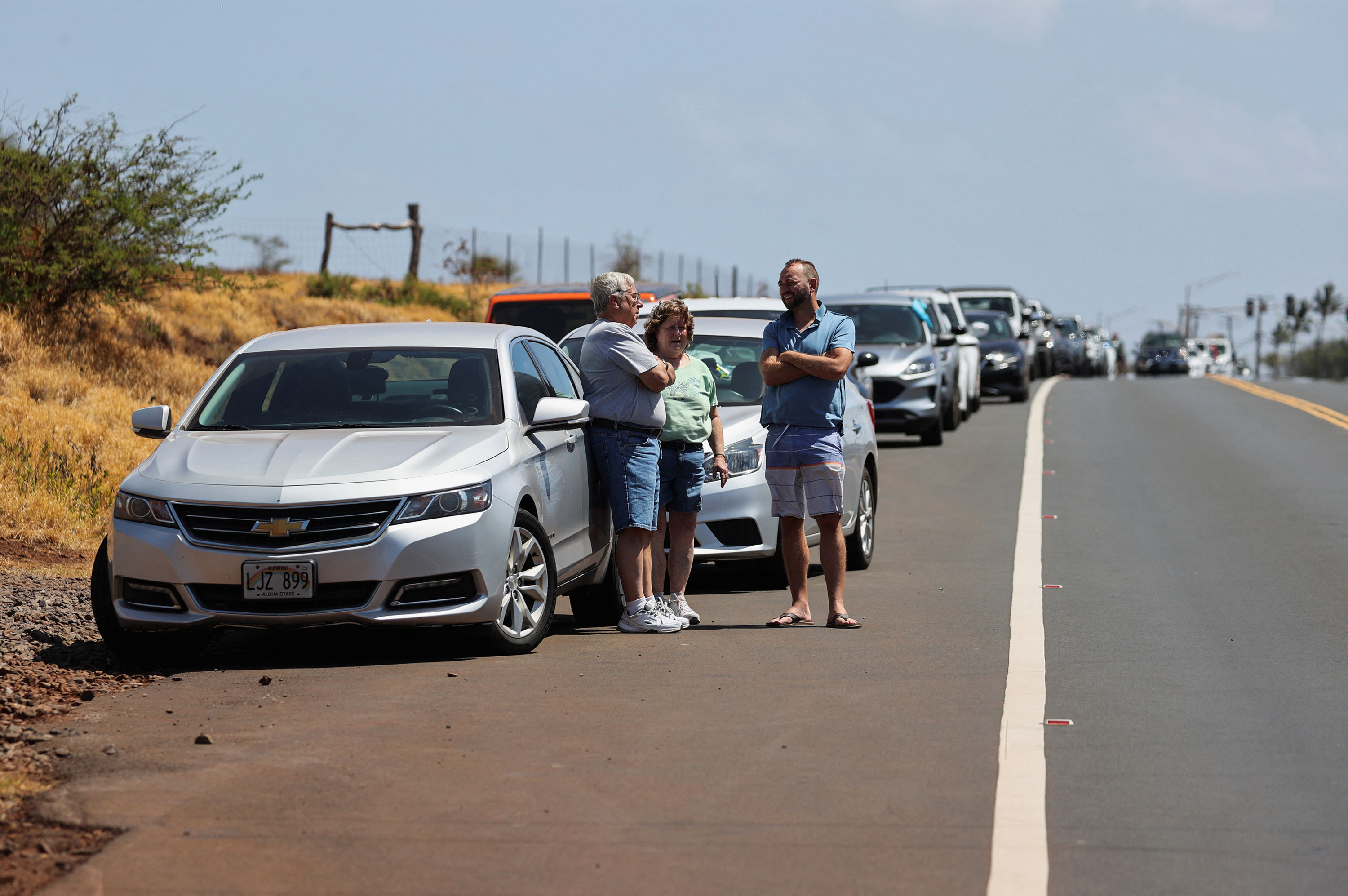 People wait on the side of the road to return to west Maui after wildfires driven by high winds were believed to have destroyed a large part of the historic town of Lahaina, in Kahului, Hawaii, on August 9, 2023.