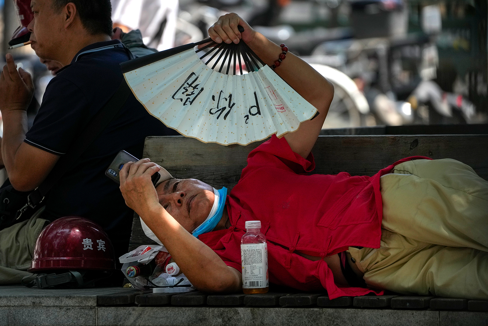 A man cools himself with a fan while browsing his phone on a hot day in Beijing, on July 16.