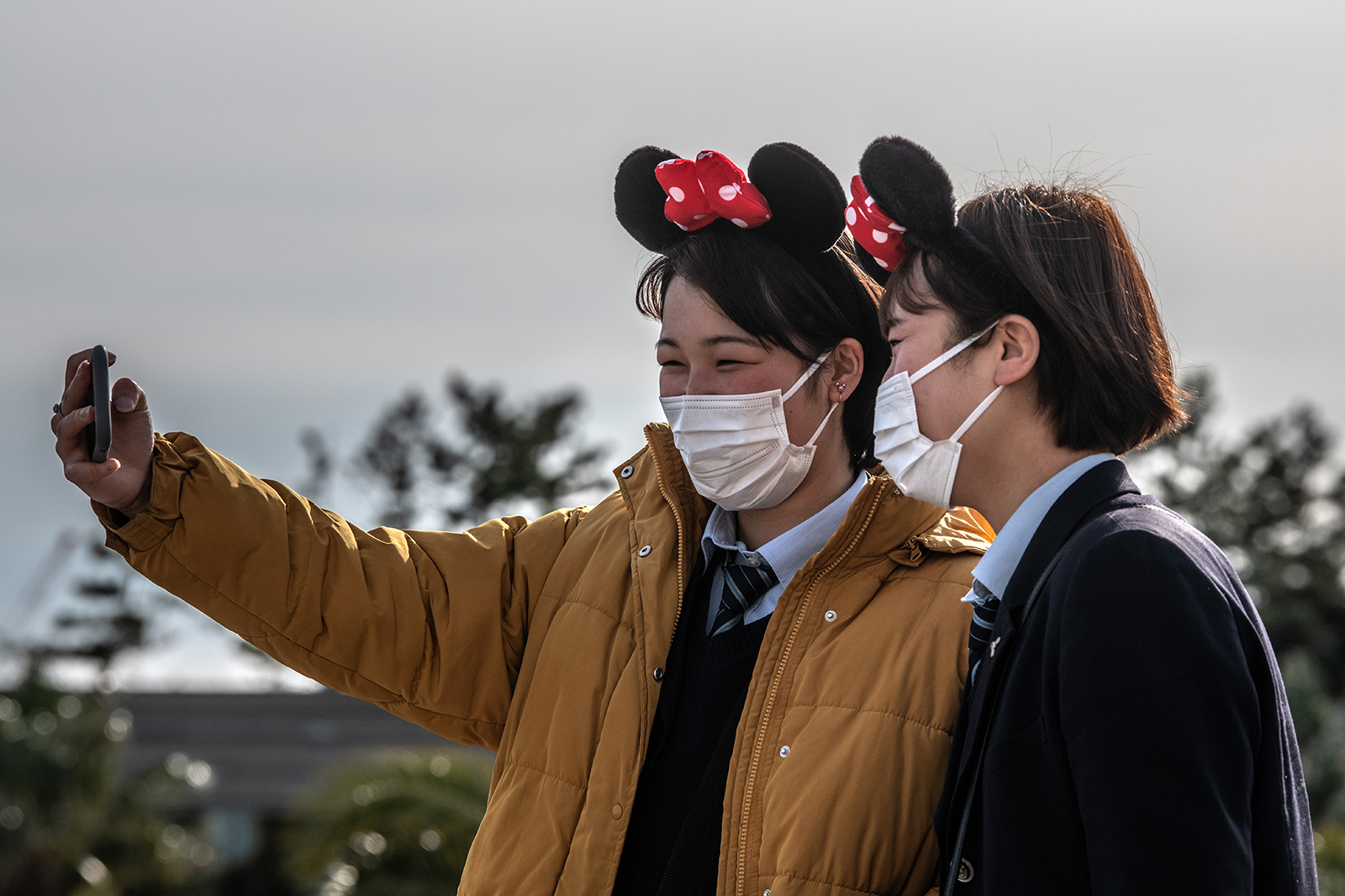 Girls wearing face masks and Disney-themed headbands take a selfie at Tokyo Disneyland on February 28, in Tokyo, Japan. 