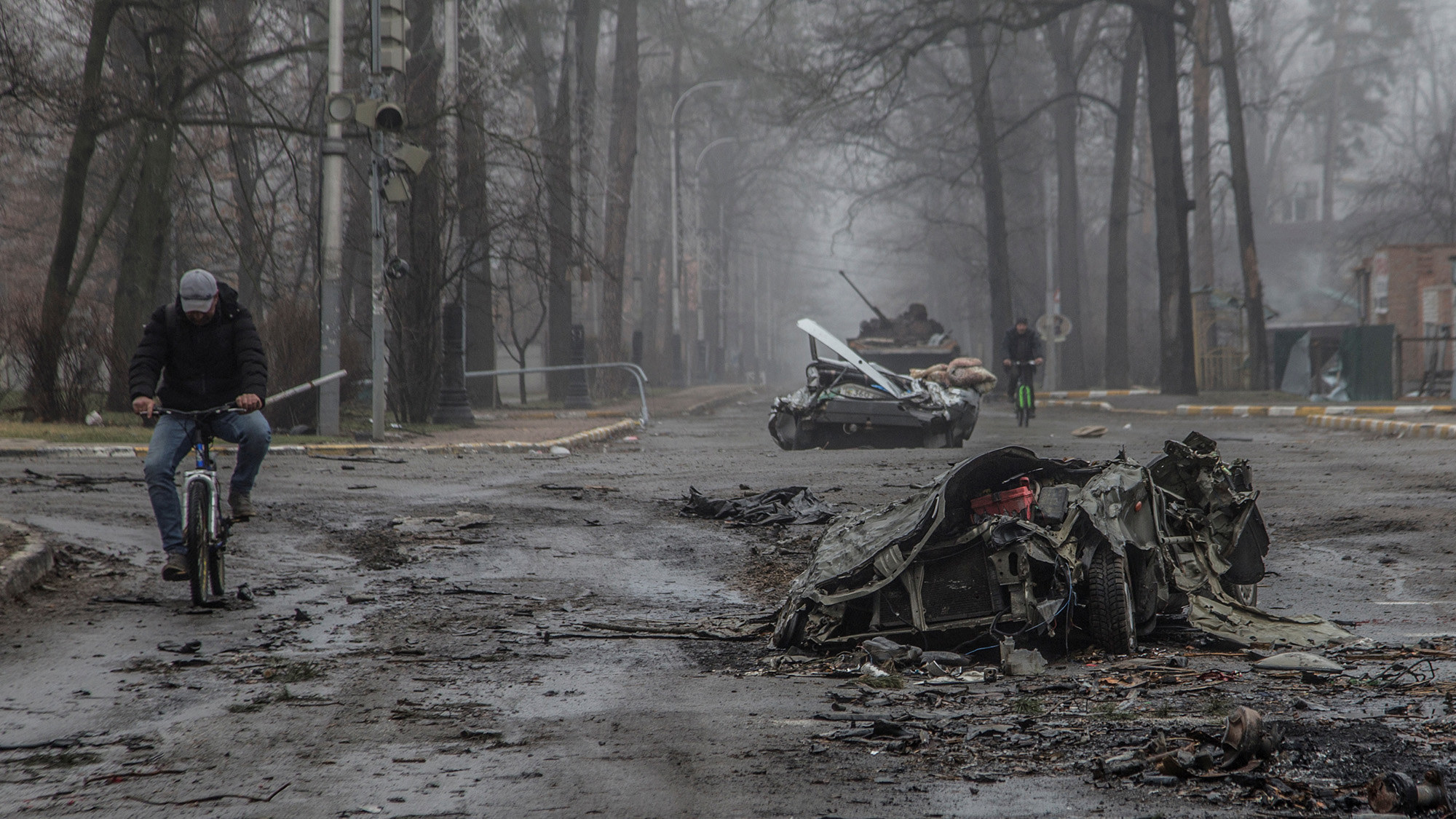Local residents ride bicycles past flattened civilian vehicles on a street in Bucha, Ukraine on April 1.
