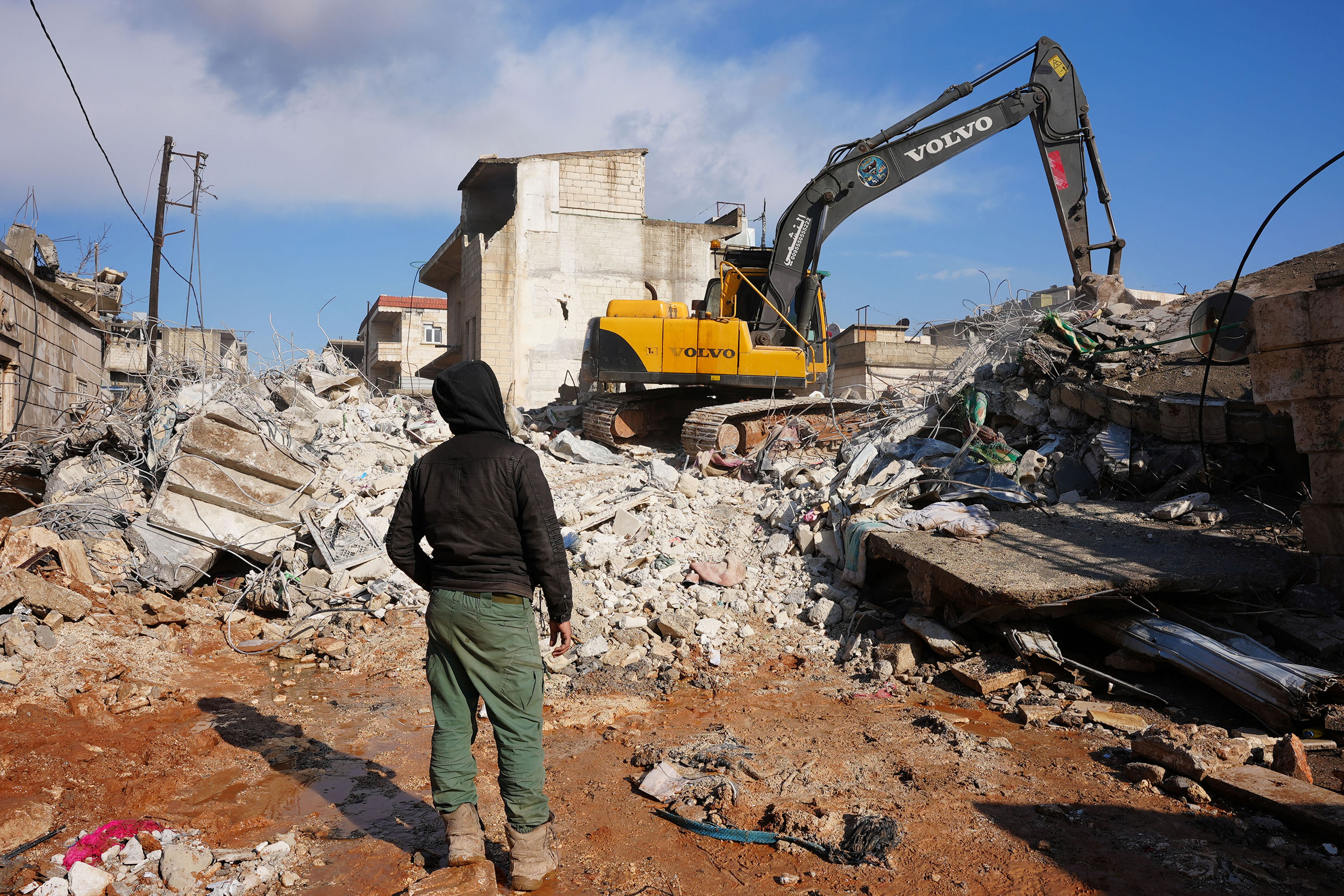A person watches as an excavator goes through the rubble of the building where the baby's family was killed.
