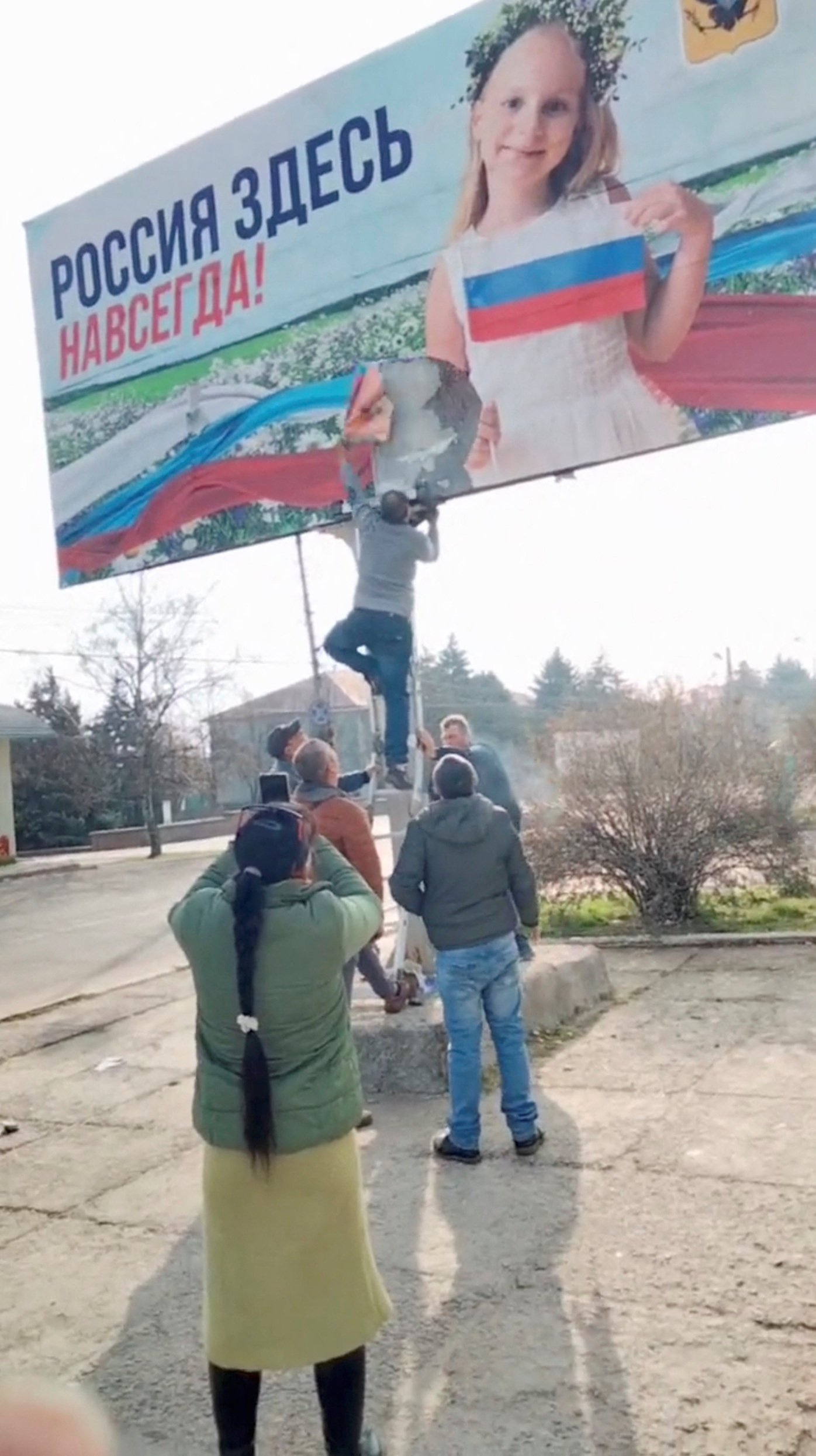 A man tears down a Russian billboard poster in Bilozerka, Kherson Oblast, Ukraine, in this still image obtained from a video released on November 11.
