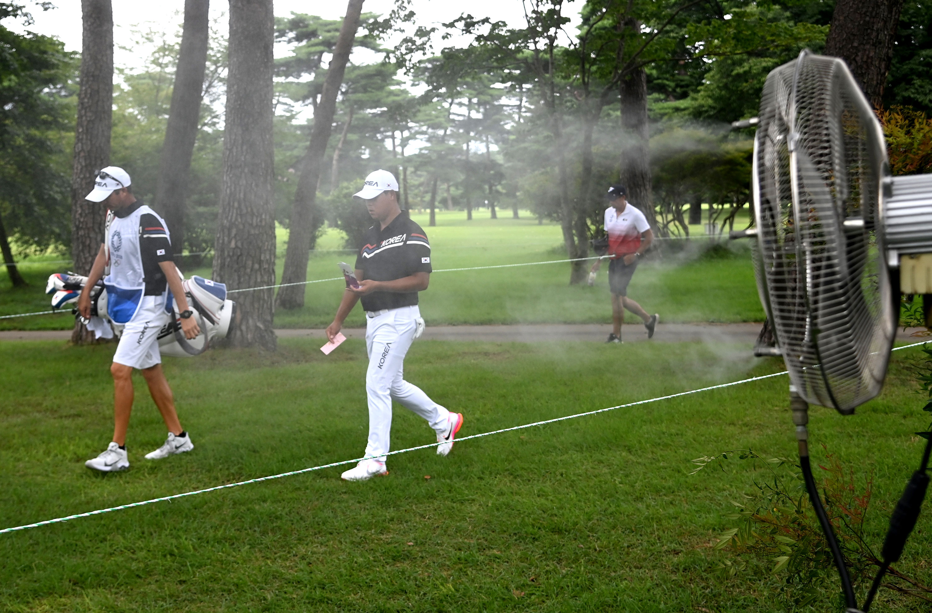 Kim Si Woo of South Korea walks past a fan spraying mist during golf competition in Kawagoe, Japan, on July 29.
