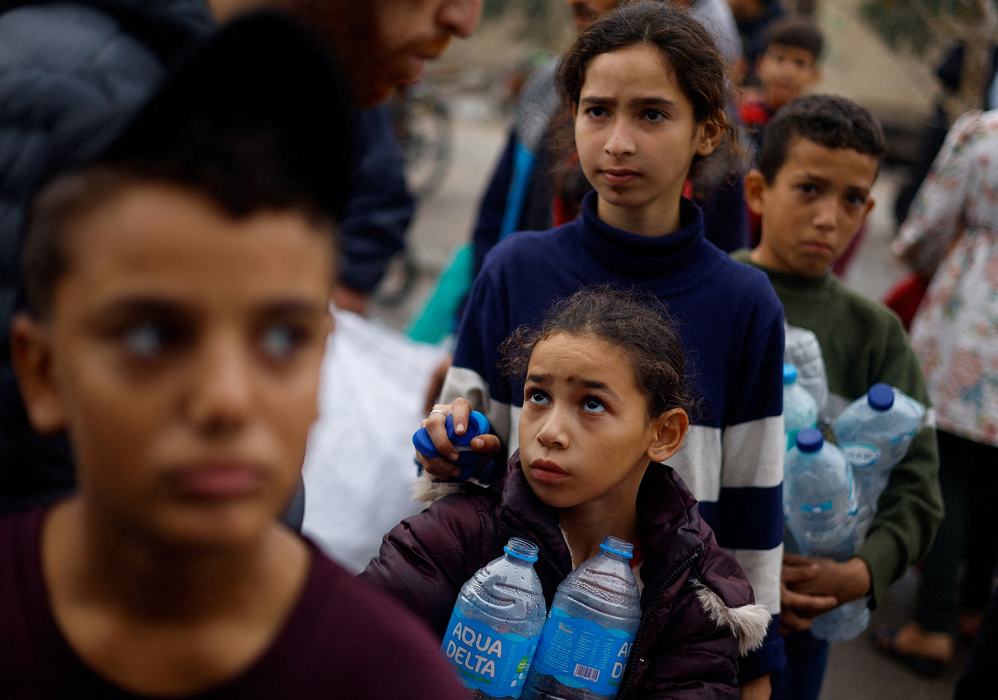 A Palestinian girl holds empty water bottles as she queues to collect water amid water shortages in Rafah, Gaza, on December 5.