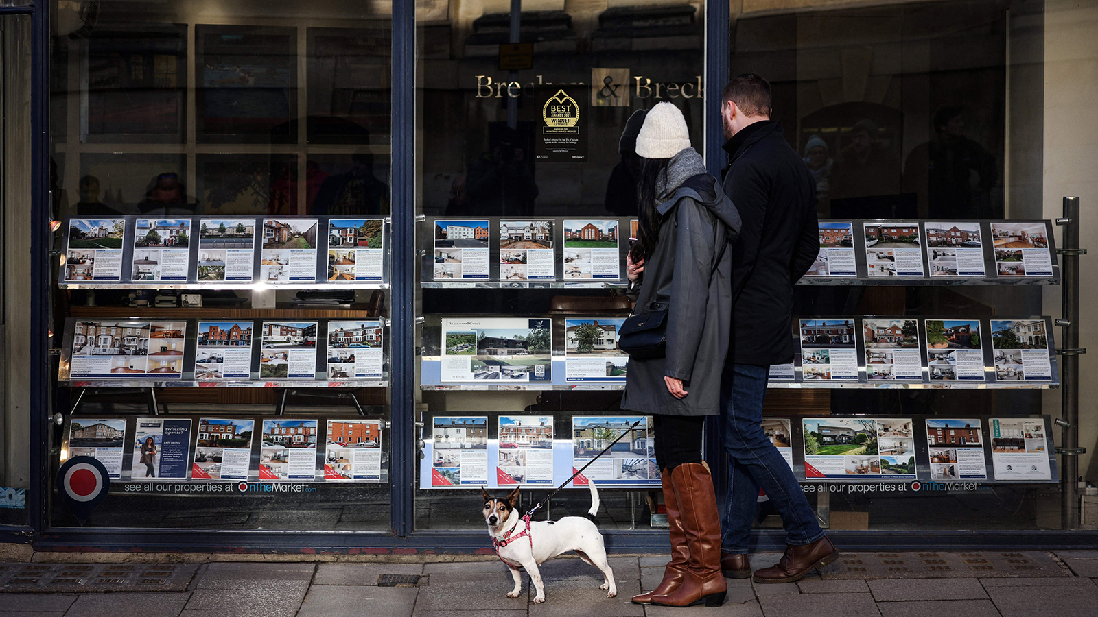 A couple with a dog look at the front window of a real estate agency displaying a selection of properties to buy or rent, in Oxford, on January 30.