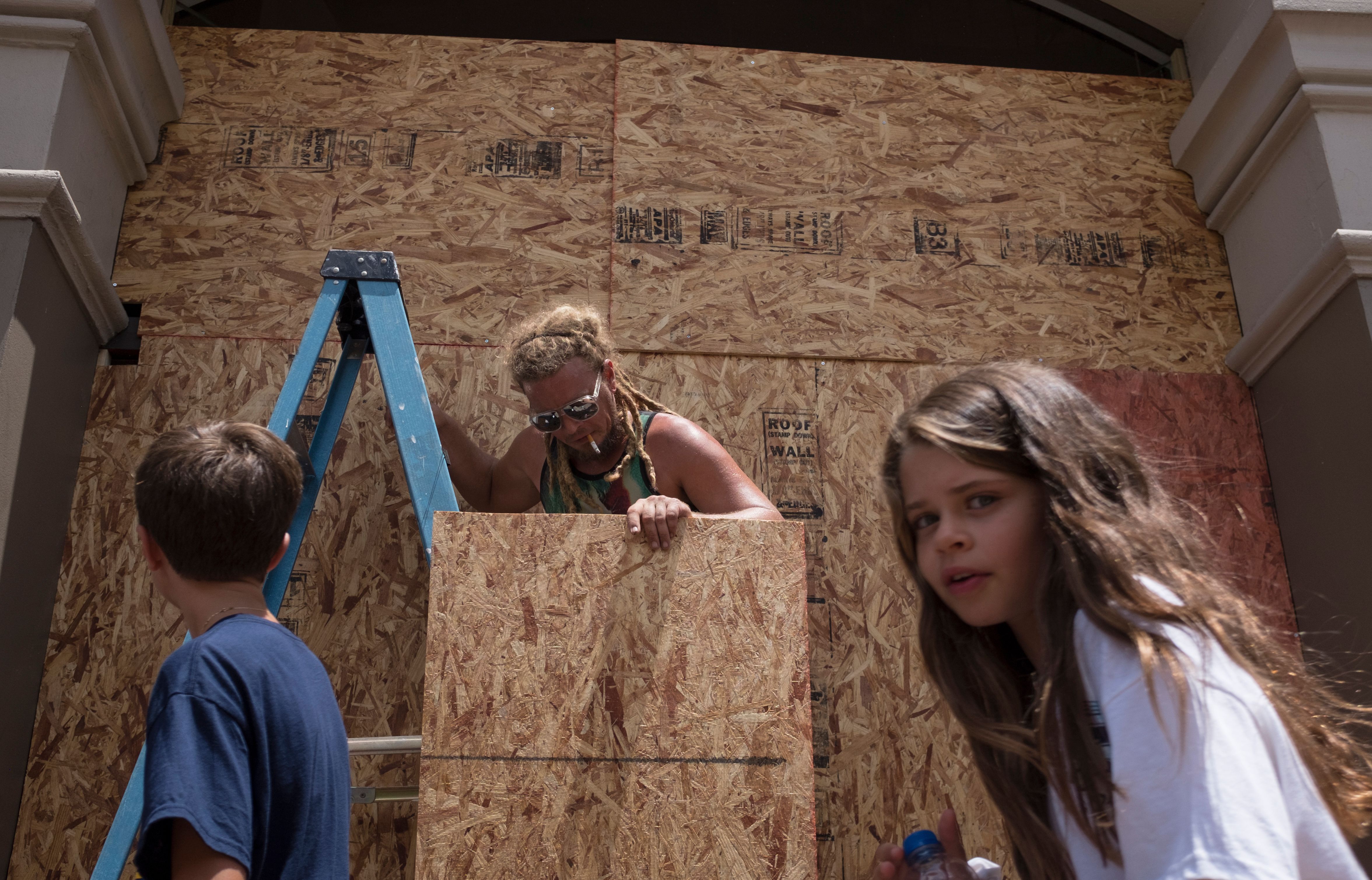 Kids walk past as Matt Harrington boards up a Vans shoe and apparel store near the French Quarter in New Orleans as tropical storm Barry approaches on July 11, 2019.