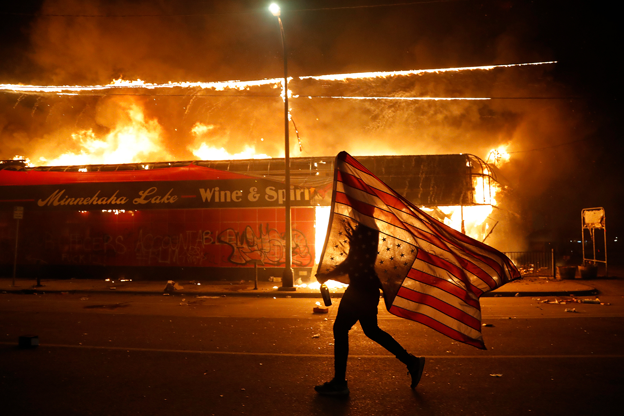 A protester carries the carries a U.S. flag upside-down, a sign of distress, next to a burning building on May 28, in Minneapolis.