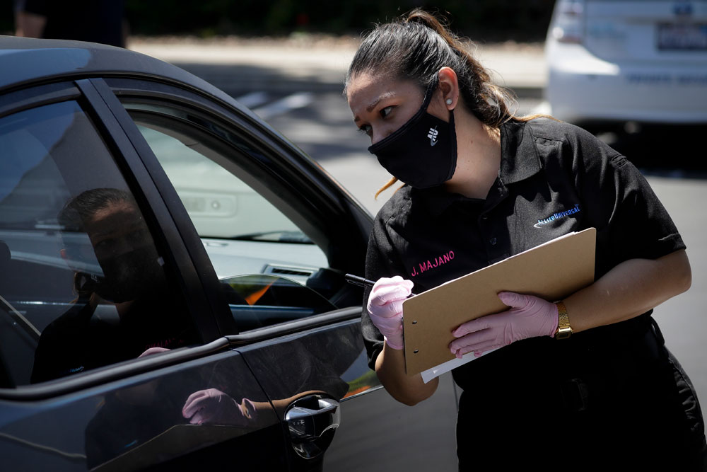 Jennifer Majano helps a job seeker fill out an application at a drive-up job fair for Allied Universal on May 6, in Gardena, California.