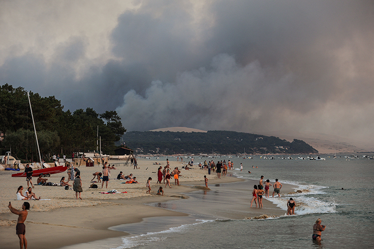 People swim on the Moulleau's beach in Arcachon, France, on Monday, July 18,  on the Moulleau's beach as the smoke rising from the forest fire in La Teste-de-Buch.