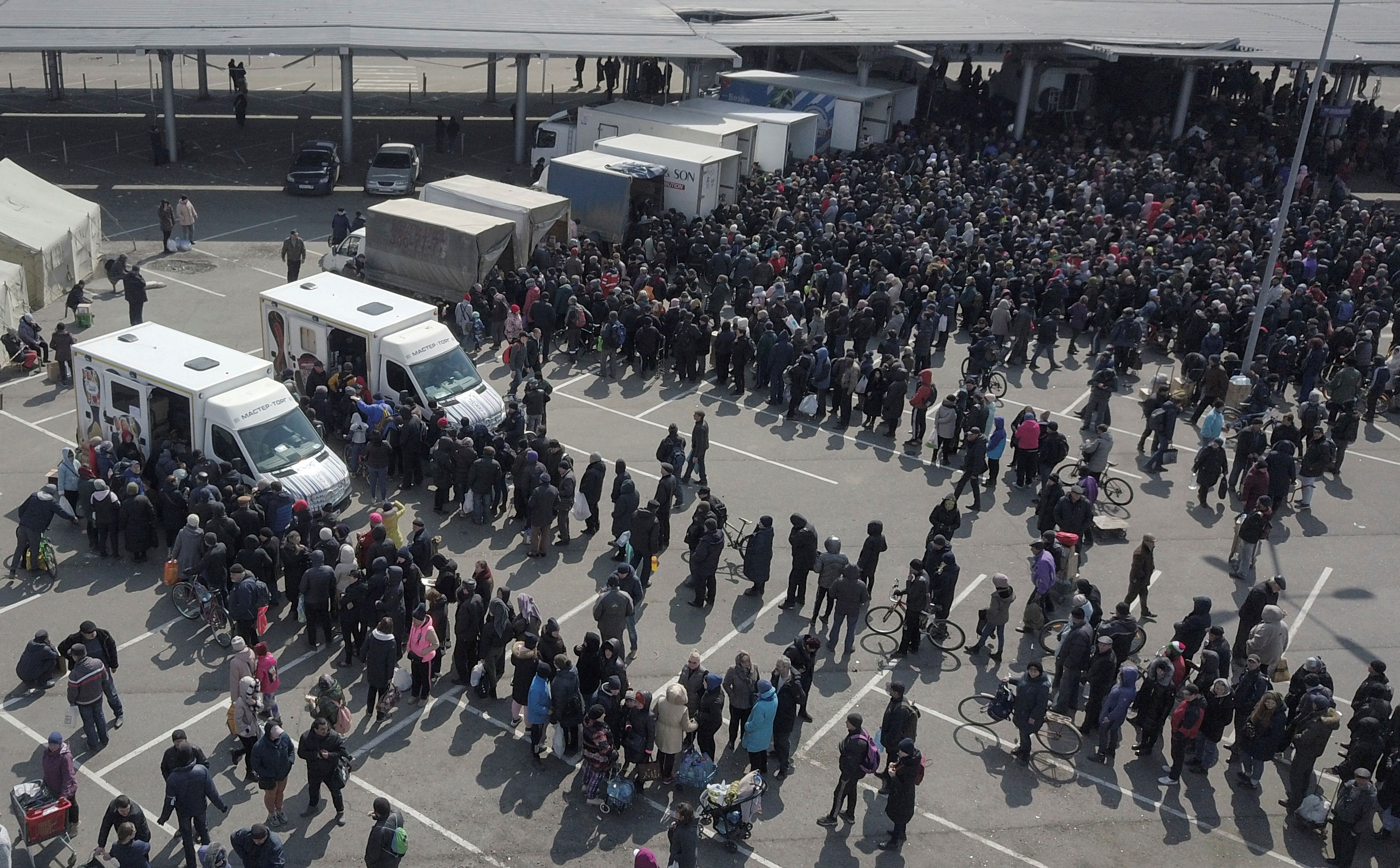 People stand in lines to buy food from mobile kiosks outside of a damaged supermarket in Mariupol, Ukraine, on Tuesday.