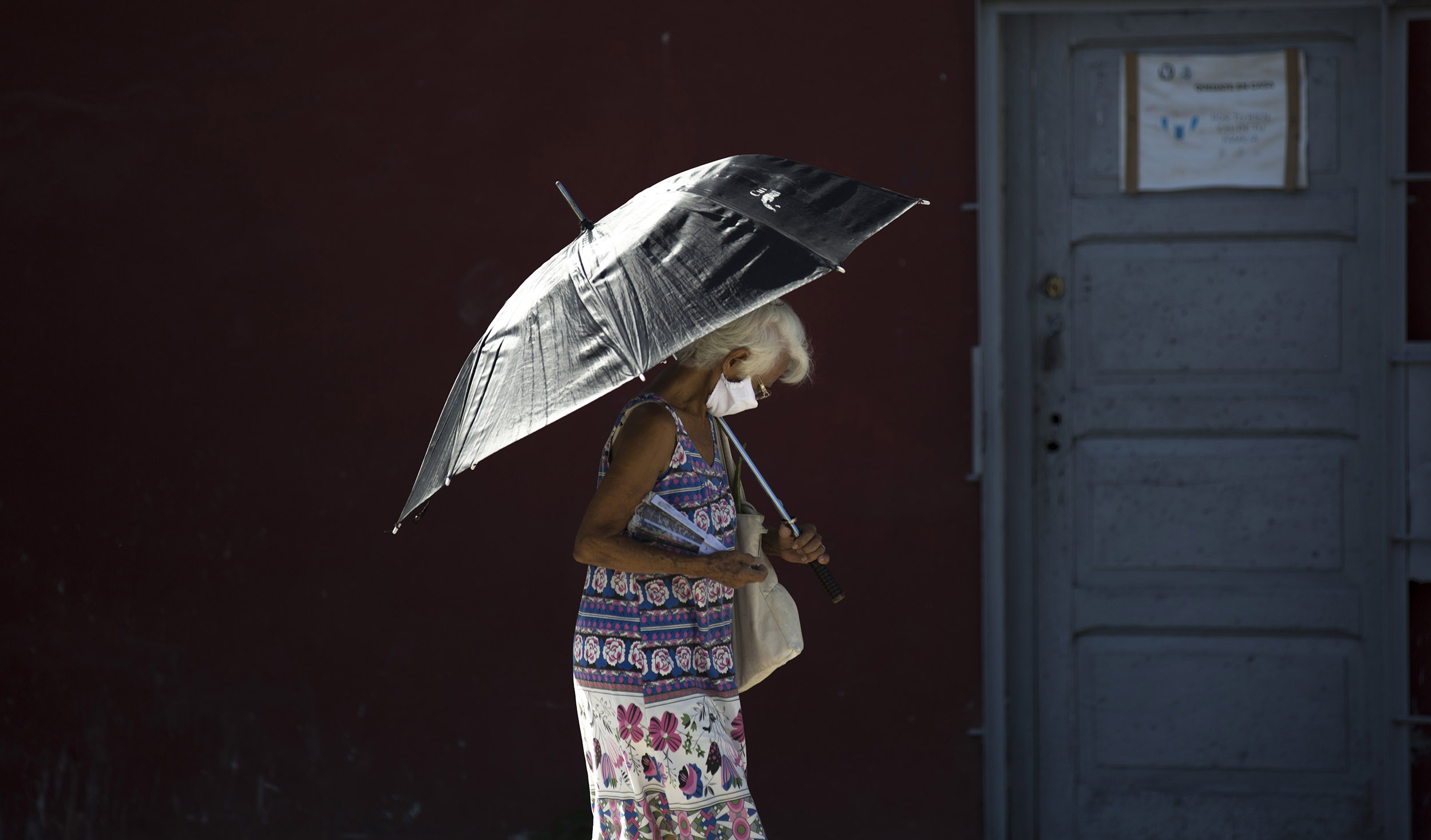 A pedestrian wearing a face mask amid the coronavirus pandemic uses a parasol in Havana, Cuba, on August 10. 
