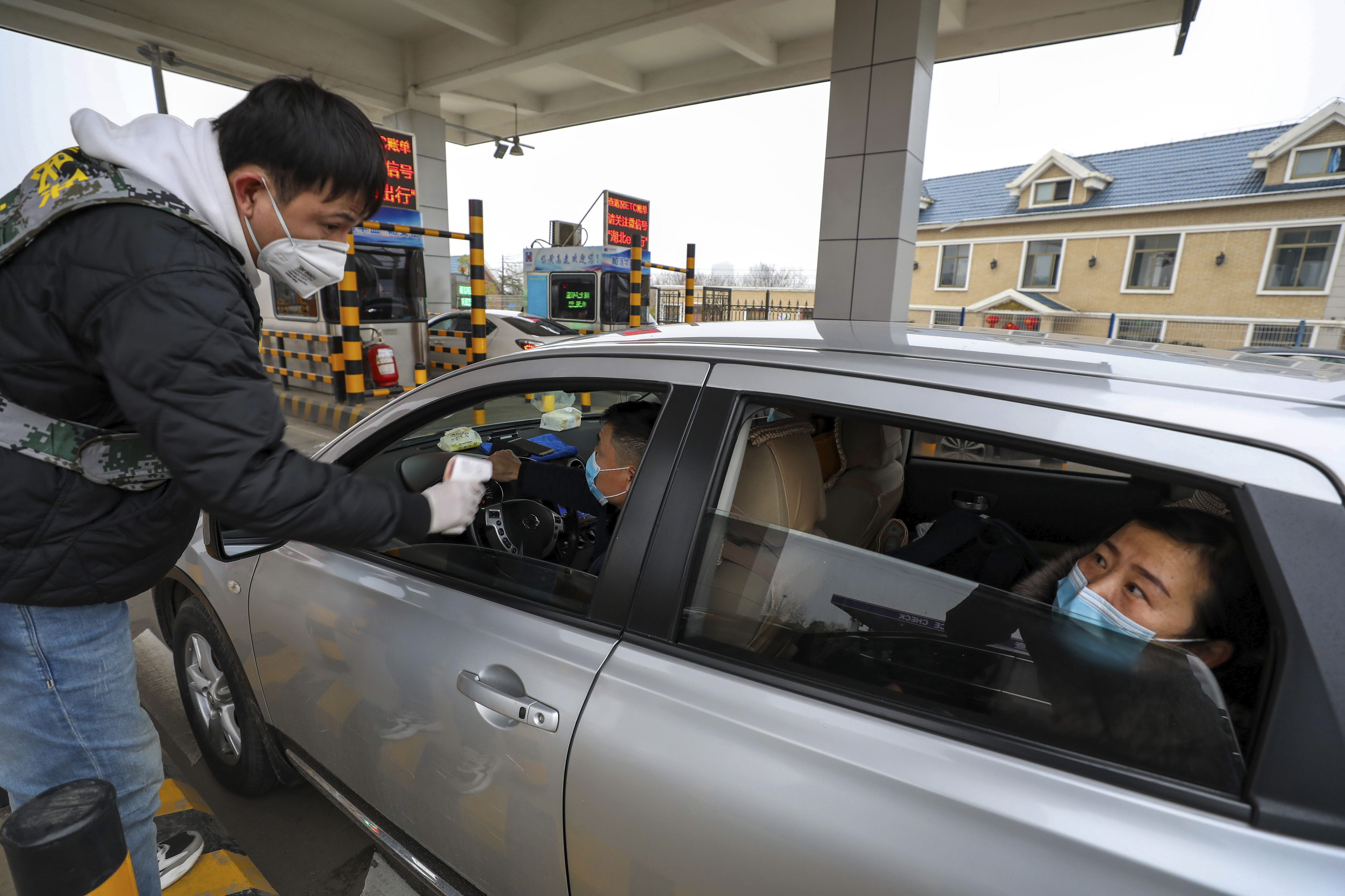 A man uses a thermometer gun to take a driver's temperature at a checkpoint at a highway toll gate in Wuhan on January 23, 2020.