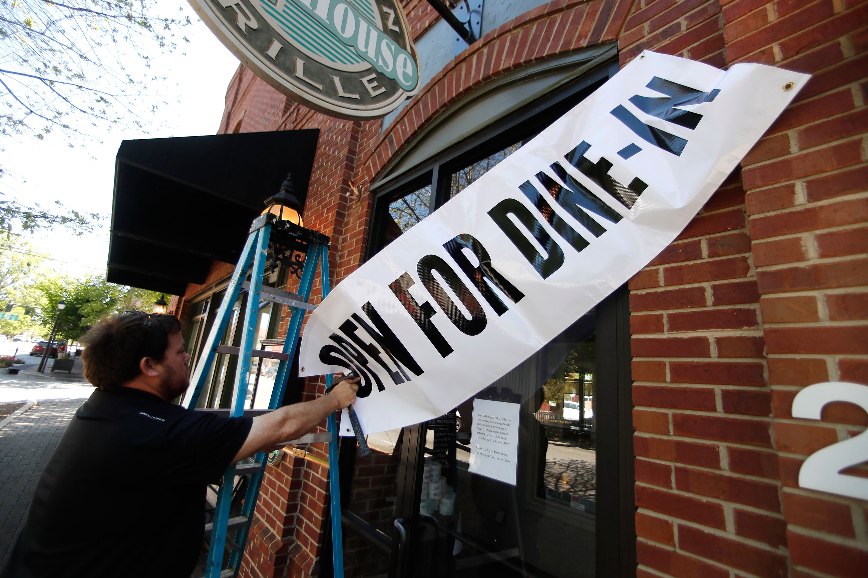 Jason Godbey hangs a banner over the entrance of Madison Chop House as they prepare to shift from take out only to dine-in service on April 27 in Madison, Georgia.
