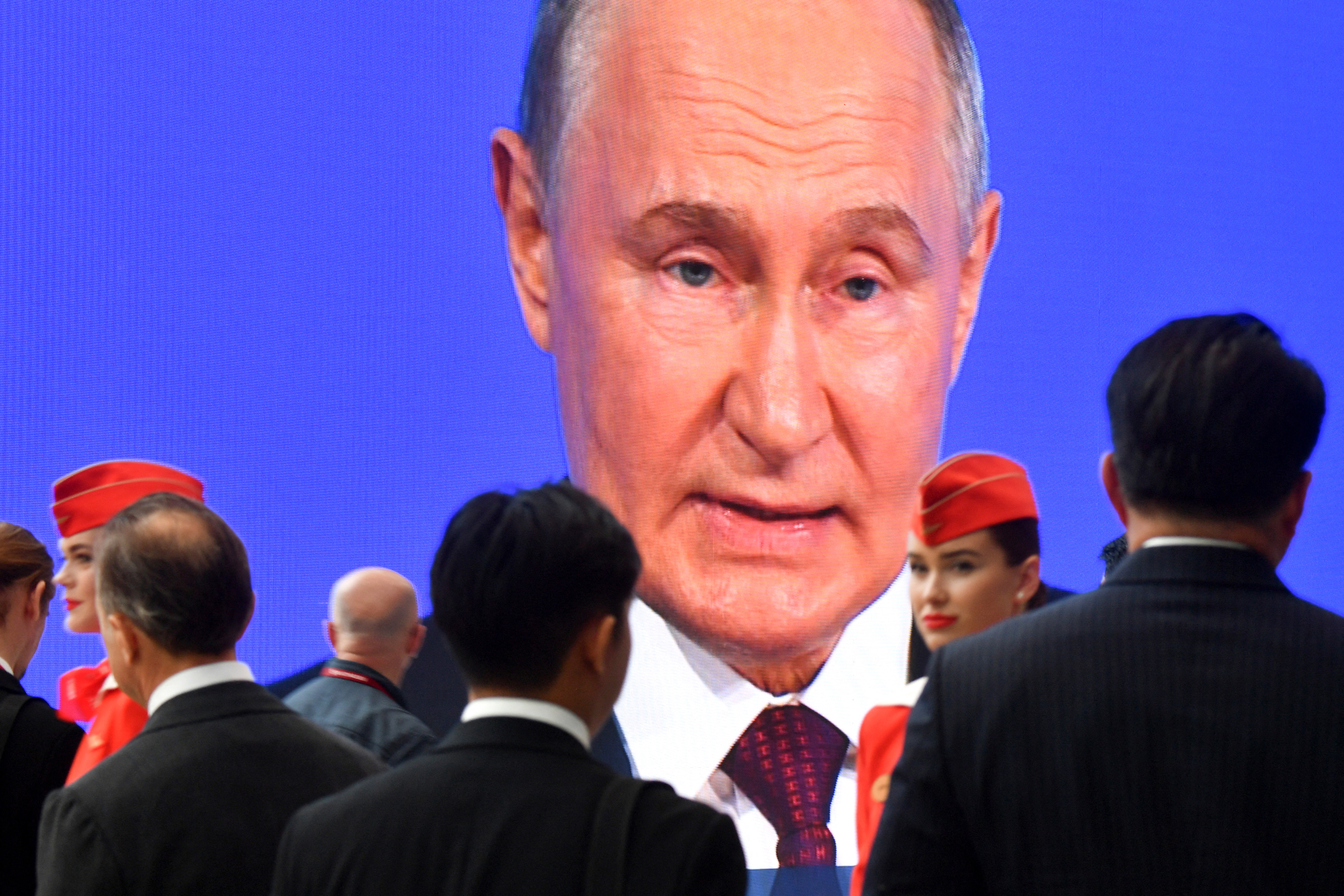 Participants stand next to a giant screen broadcasting Russian President Vladimir Putin's address during the Saint Petersburg International Economic Forum in Saint Petersburg, Russia, on Friday.