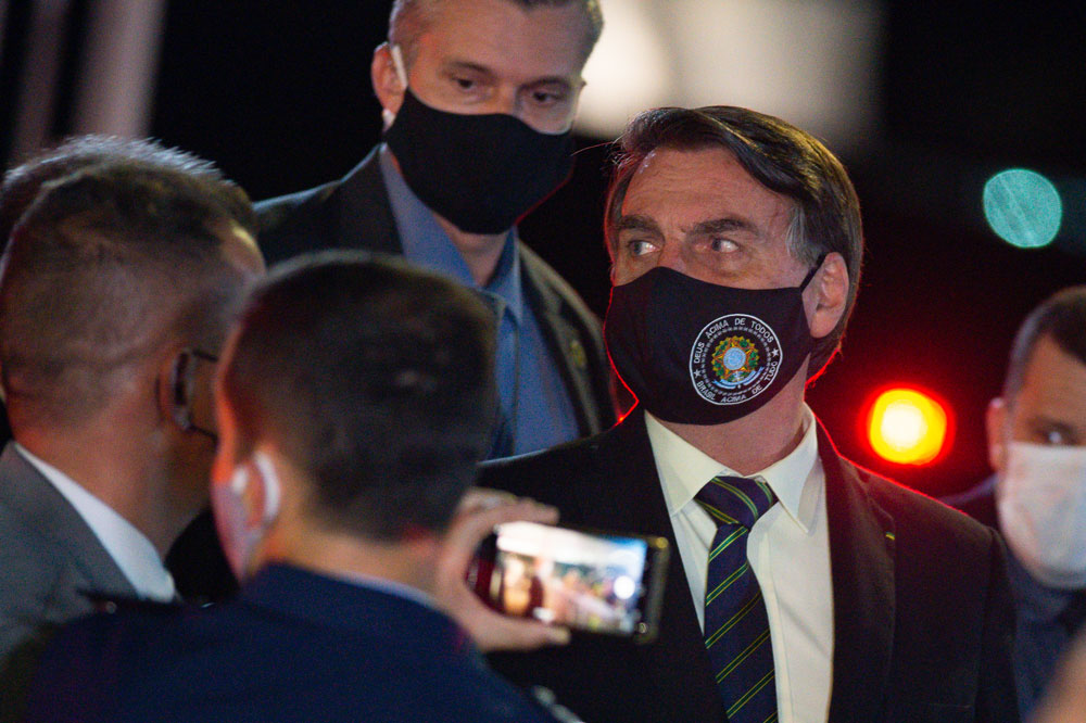 President of Brazil Jair Bolsonaro, wearing a face mask with a print of Brazil's Coat of Arms and written God above all, Brazil above all, watches supporters of his government who waited for him outside the Palácio do Alvorada on May 27 in Brasilia. 