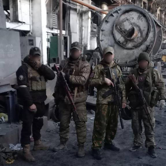 Fighters from the Wagner private military company pose for photographs in what appears to be a workshop within the AZOM metallurgical plant in Bakhmut, Ukraine. The fighters’ faces were previously blurred in this version of the image taken from Telegram.