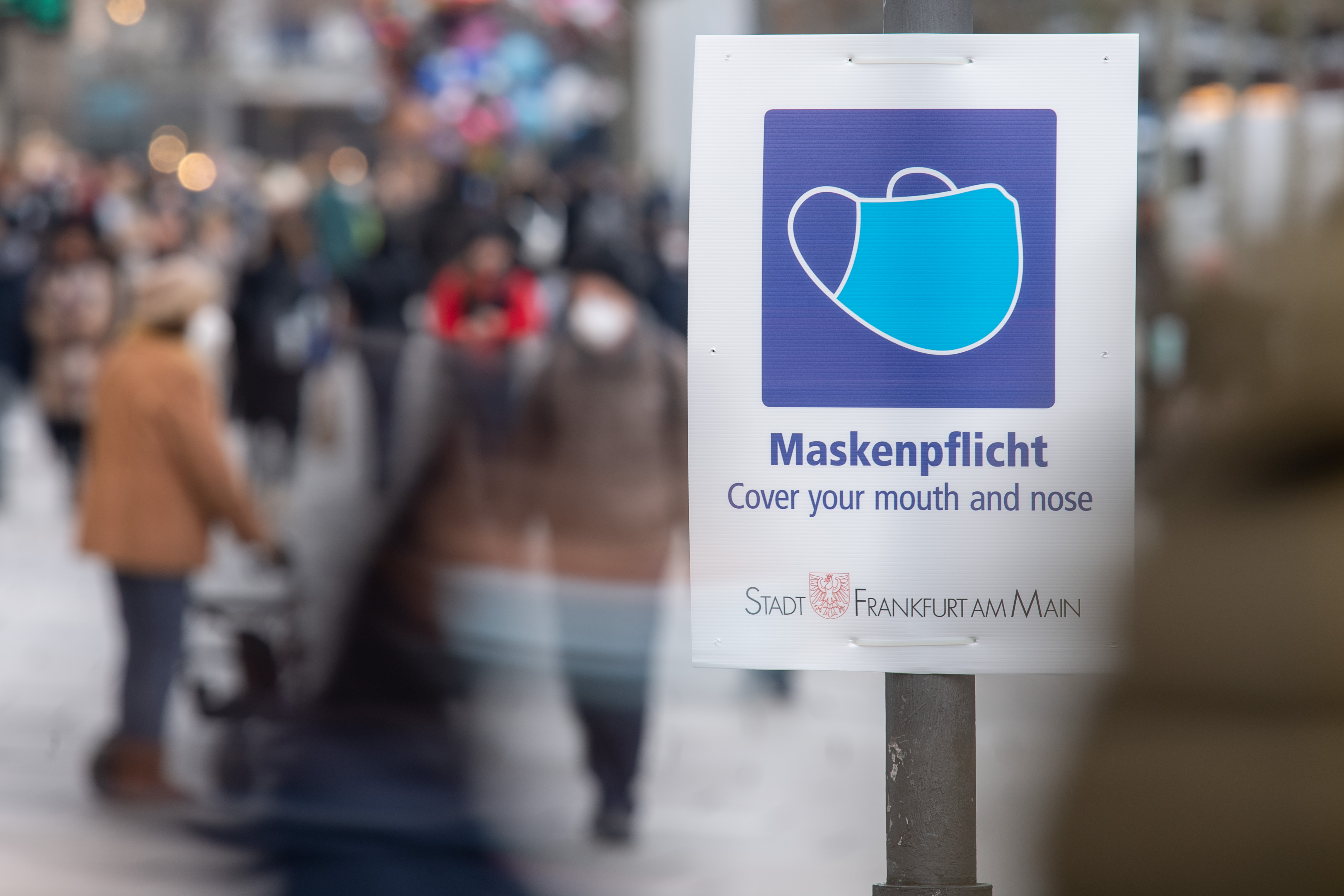 A sign reminds pedestrians along a shopping center in Frankfurt, Germany, on Monday, January 17, 2022 that mask wearing are mandatory to be worn out in public.