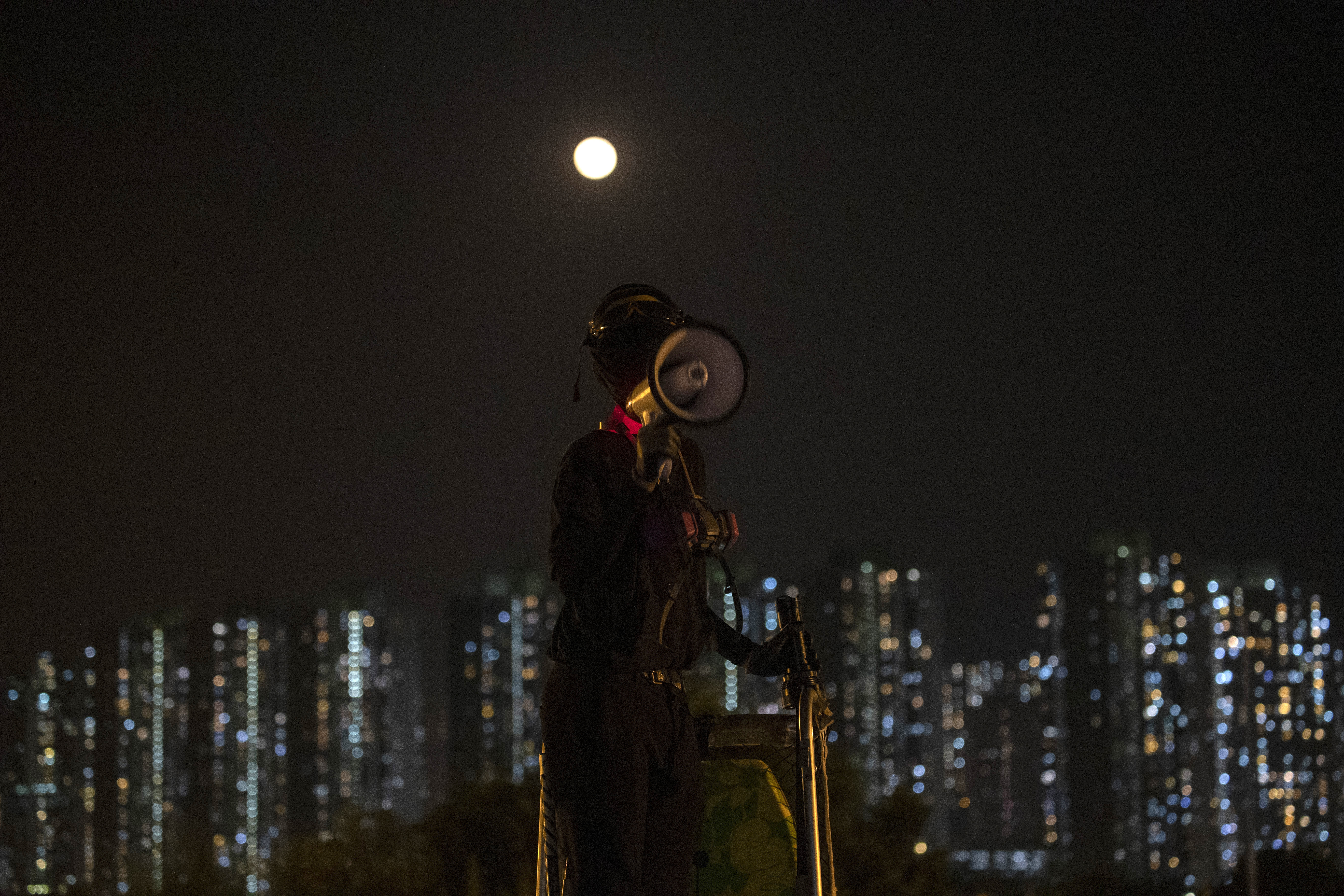 A protester speaks over a loud megaphone as a full moon rises over the barricaded bridge into the Chinese University of Hong Kong on Wednesday night. 