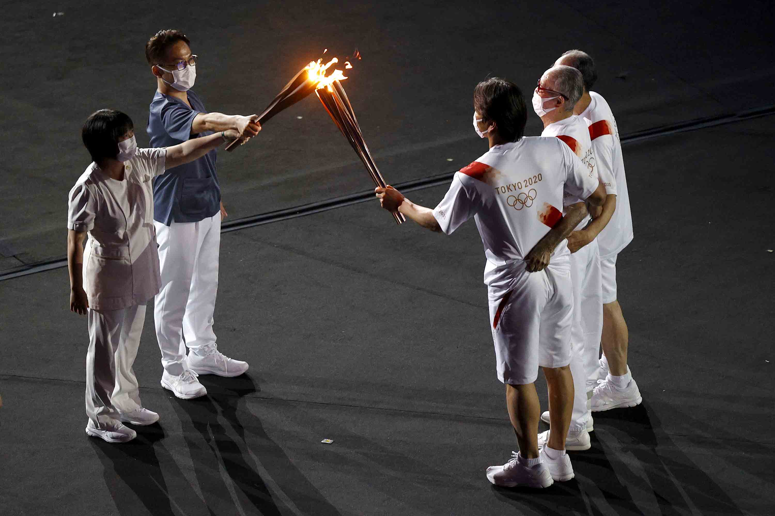 Torch carriers exchange the flame of the Olympic torch during the Opening Ceremony.