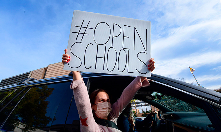 Signs calling for schools to reopen are displayed by people in passing vehicles during an "Open Schools Now" rally in Los Angeles on February 15, 2021.