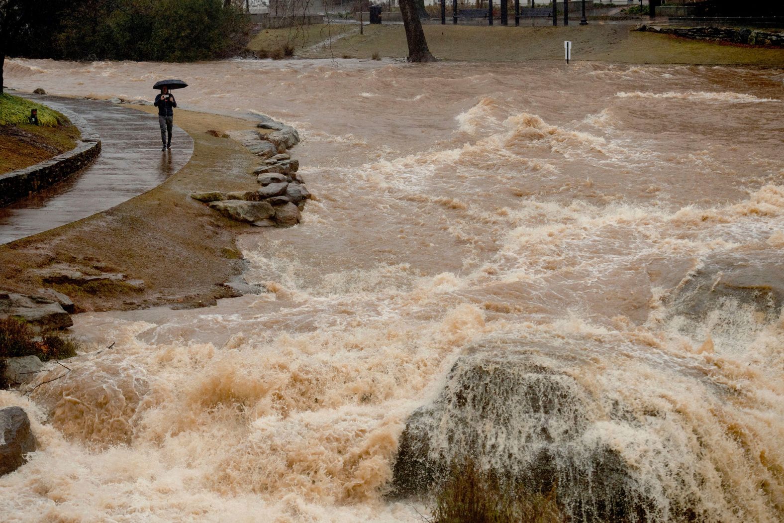A man braves the rain Tuesday while taking videos of the Reedy River's rushing water in Greenville, South Carolina.