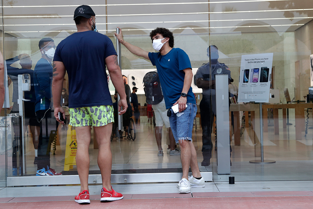 An employee wearing a protective face covering, right, monitors the flow of customers at an Apple retail store along Lincoln Road Mall during the new coronavirus pandemic on Wednesday, June 17, in Miami Beach.