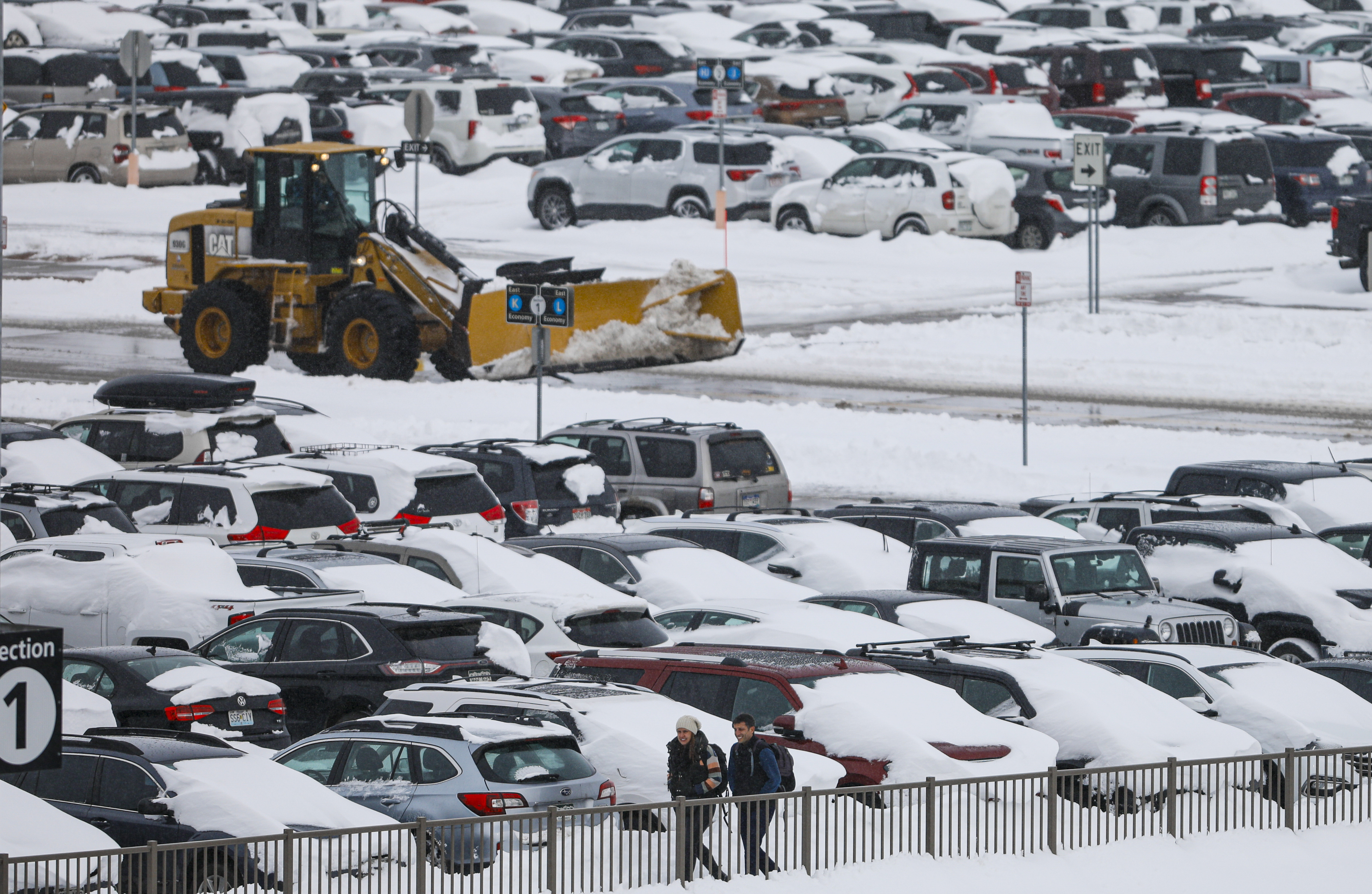 People walk past snow-covered cars parked as a plow clears roadways at Denver International Airport on November 26, 2019 in Denver, Colorado.