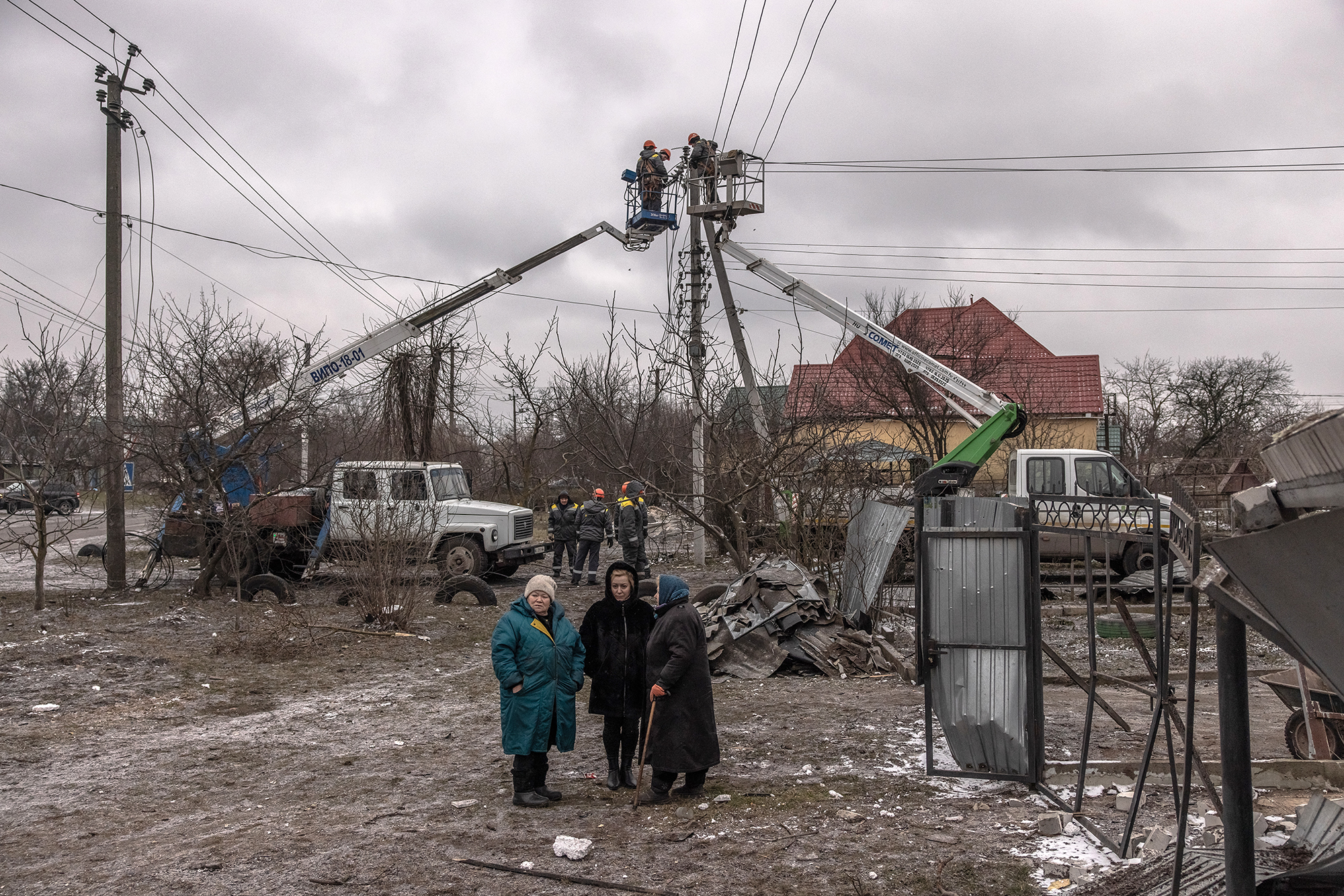 Women stand next to damaged residential houses as workers repair electricity cables following Russian missile attacks on January 26, in Hlevakha, outside Kyiv, Ukraine. 