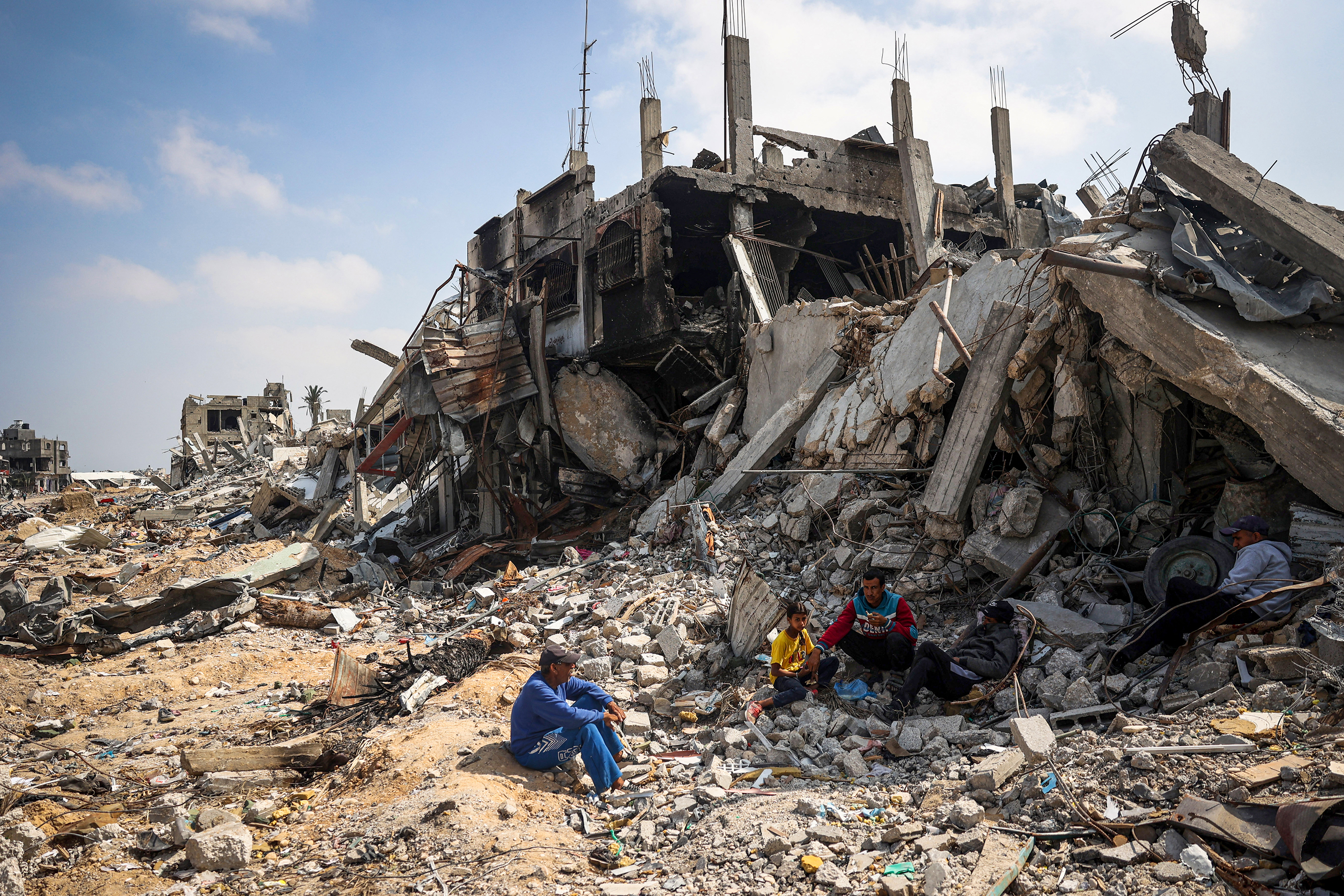 People sit on the rubble of buildings destroyed during Israeli bombardment in Khan Younis,
