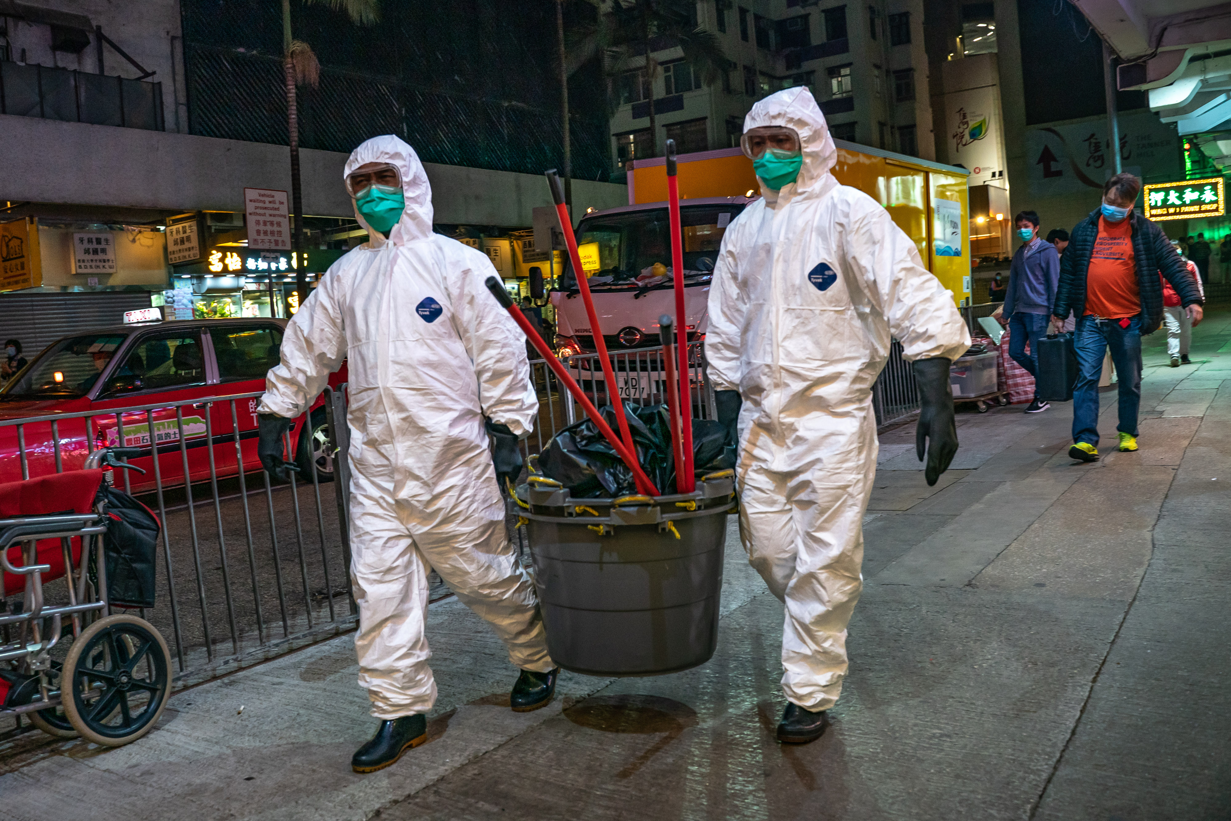 Workers wearing protective equipment carry cleaning supplies into a residential building in Hong Kong.