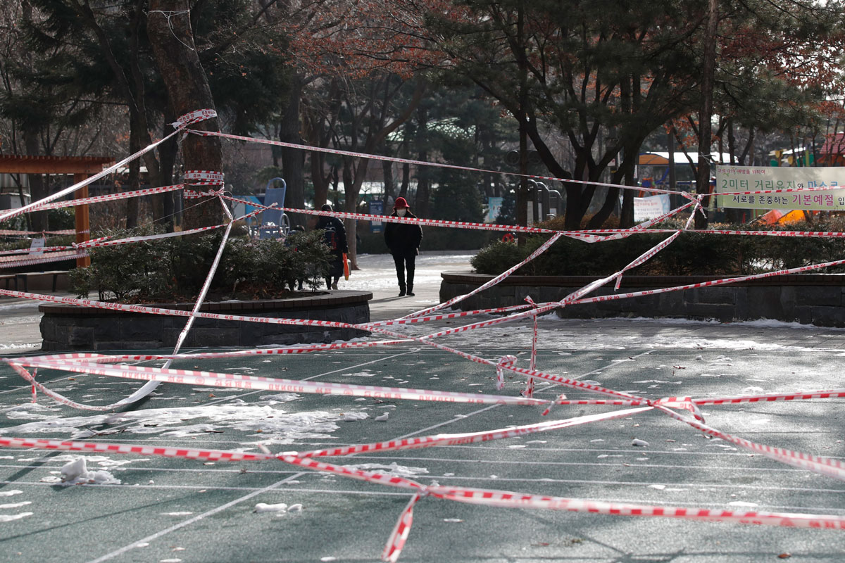 Seorang wanita yang memakai masker wajah berjalan di dekat taman yang terdaftar untuk mematuhi langkah-langkah jarak sosial di Seoul, Korea Selatan pada 14 Januari.