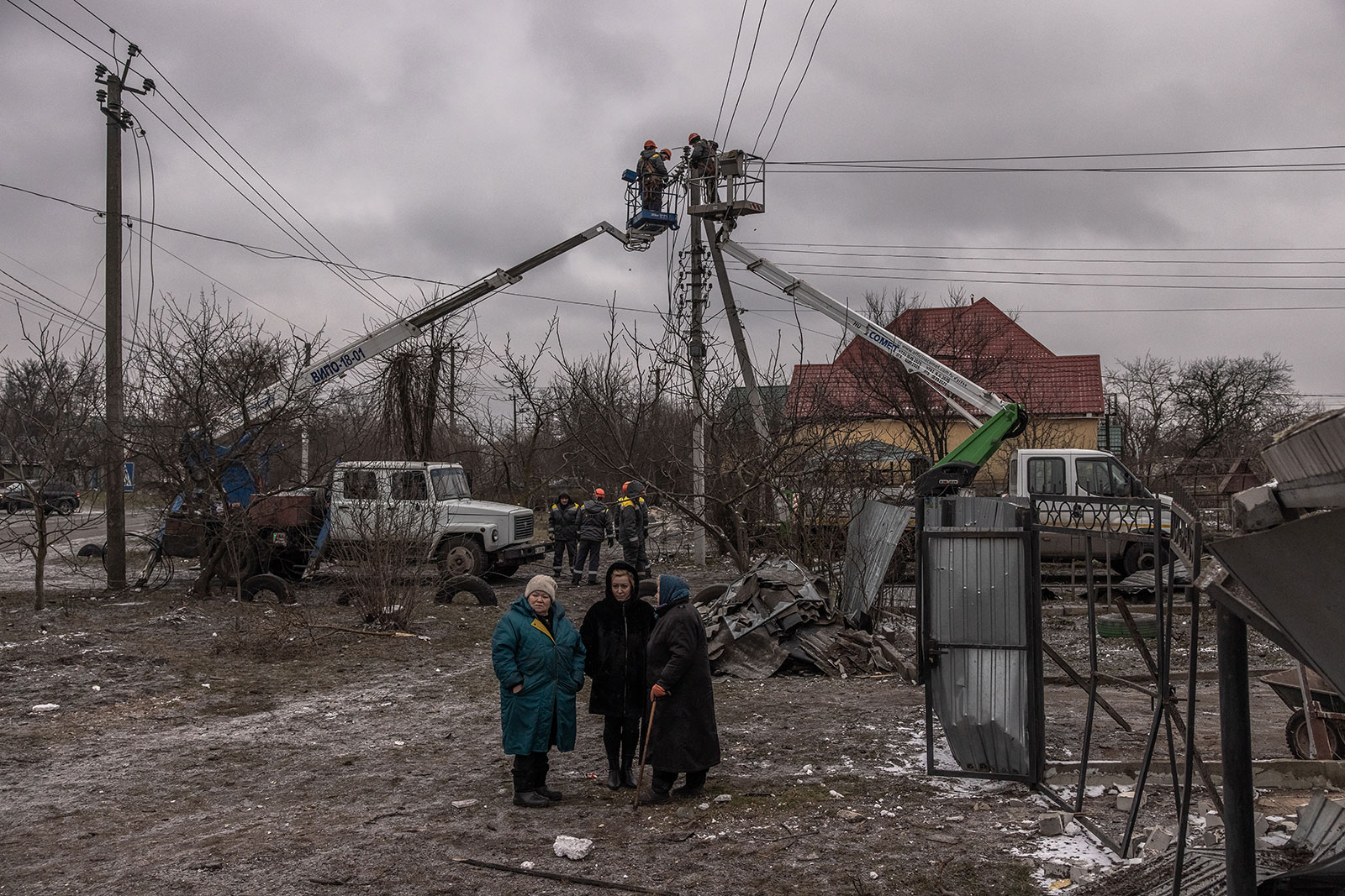 Women stand next to damaged residential houses as workers try to repair electricity cables following Russian missile attacks on January 26 outside of Kyiv, Ukraine.