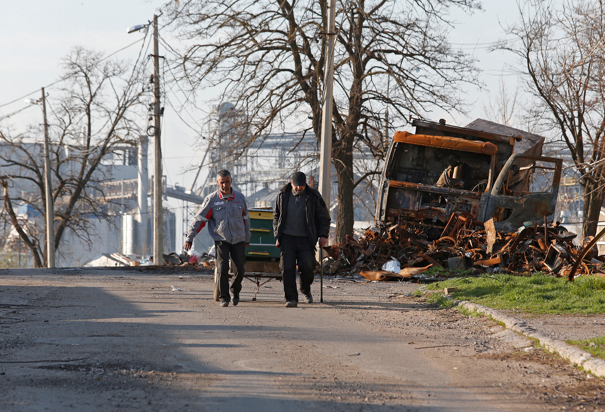 Local residents walk past a destroyed vehicle in the southern port city of Mariupol, Ukraine, on April 20.