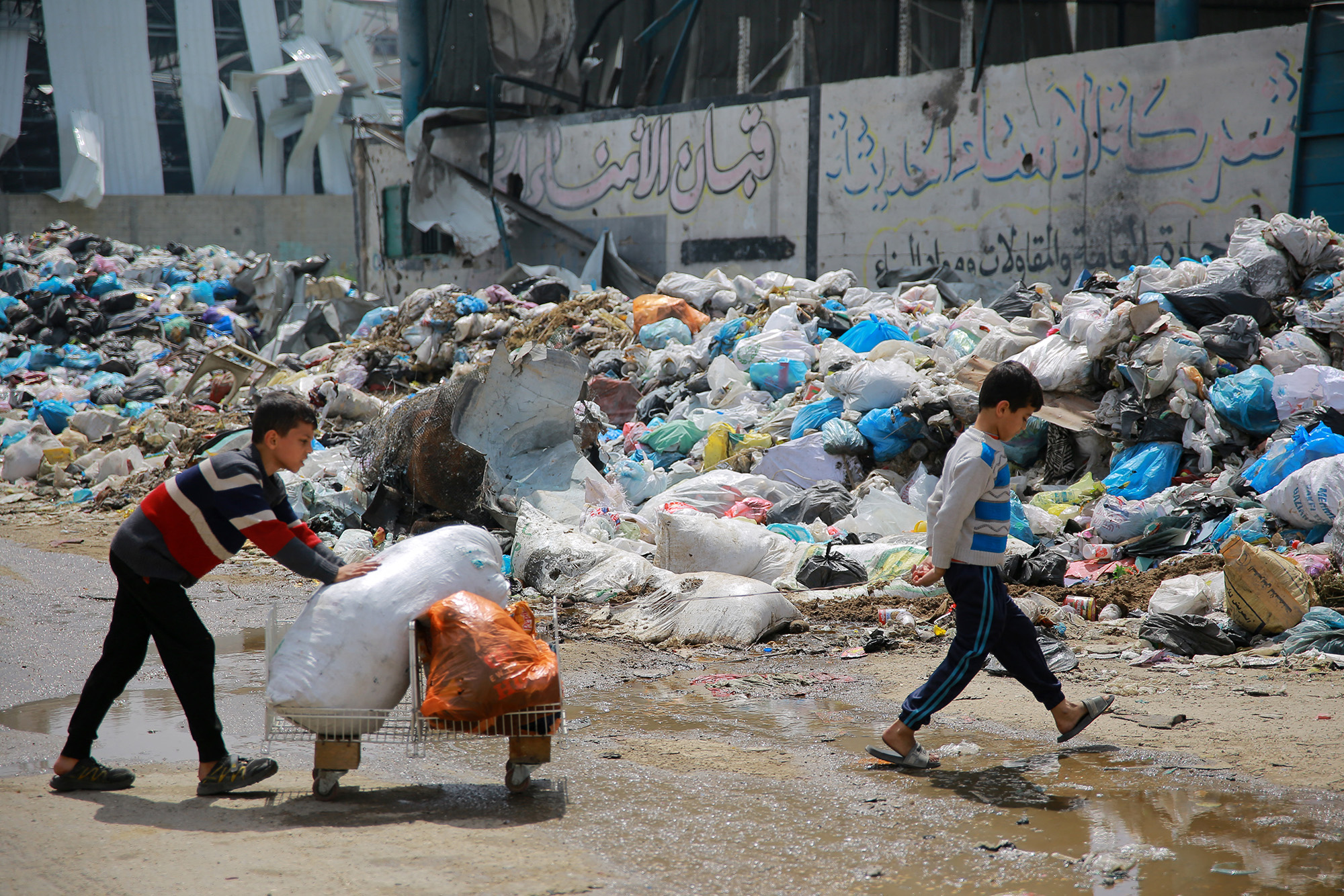 Children walk past a pile of household refuse in a street in Gaza on March 28.